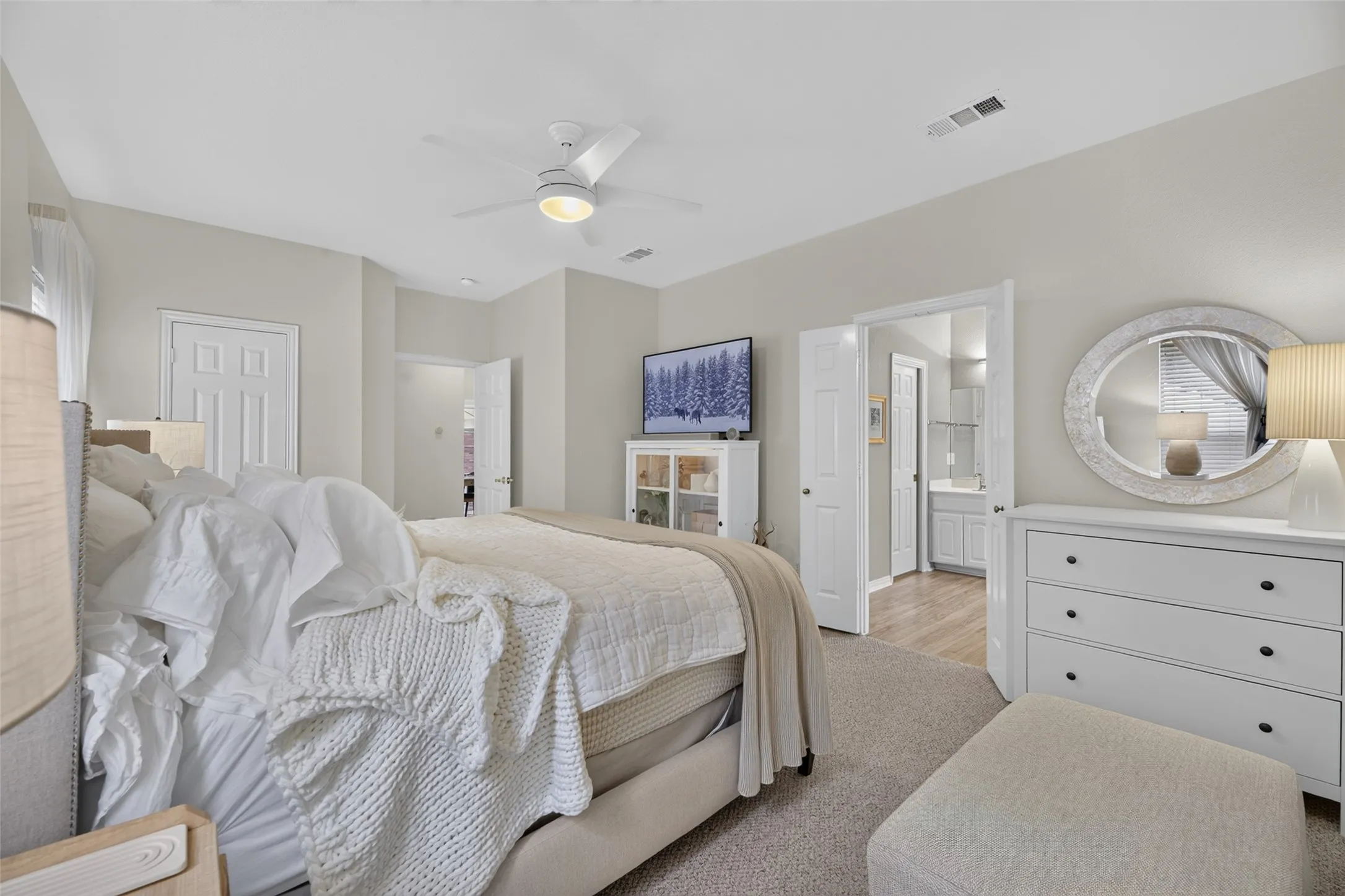 Carpeted bedroom with a ceiling fan, light gray painted walls, a white paneled door, and an entryway to an adjoining bathroom featuring wood-finish flooring