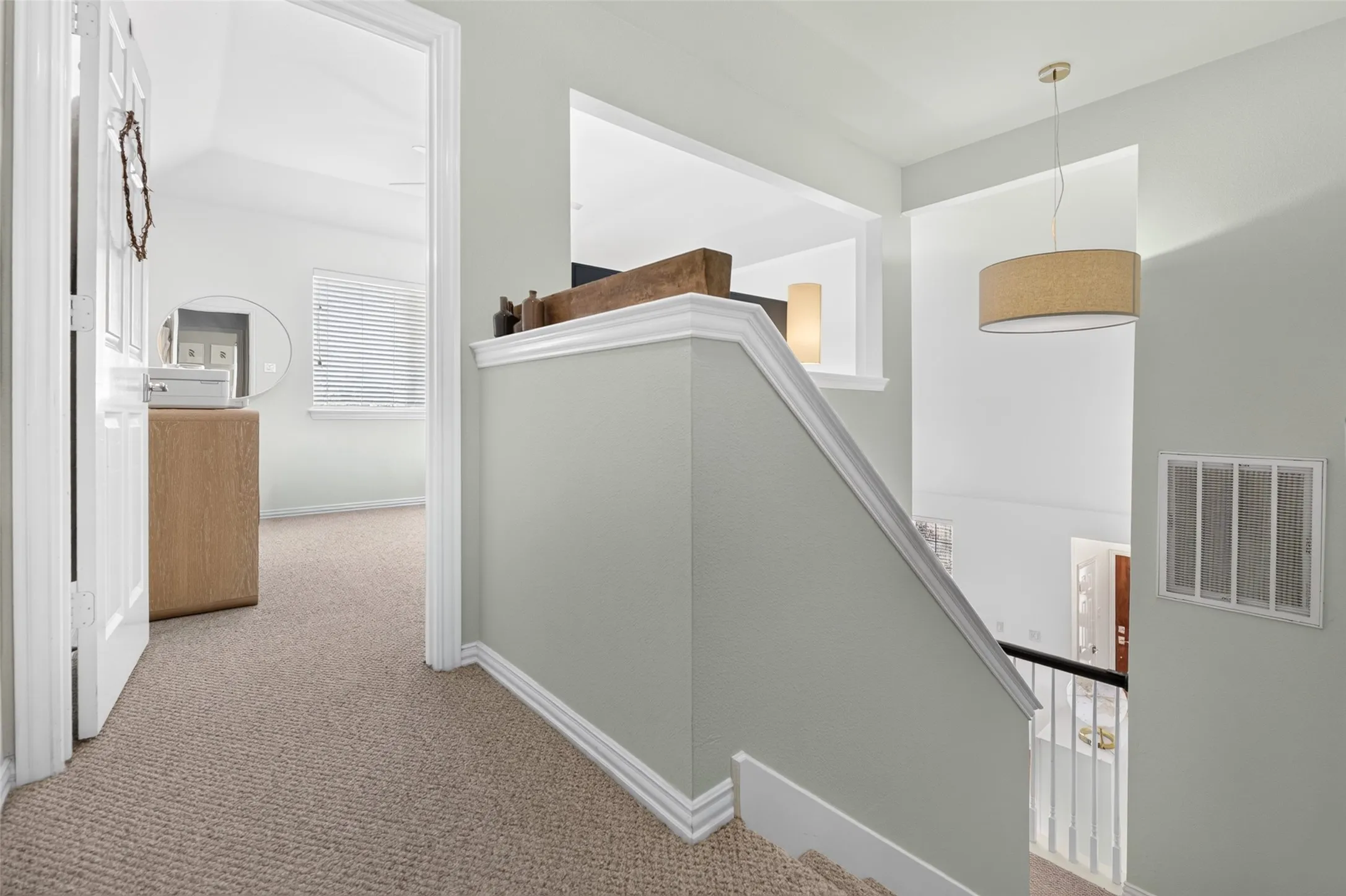 Carpeted hallway with a staircase featuring a white railing and banister