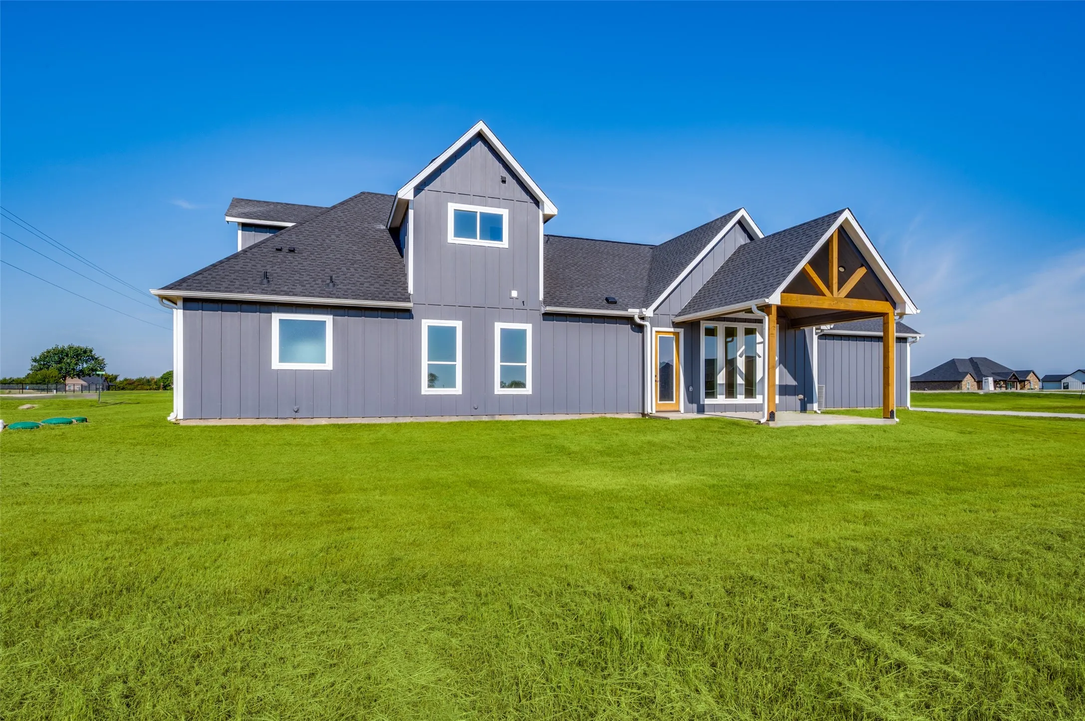 Modern farmhouse architecture with vertical siding, gabled rooflines, a covered patio with exposed wood beams, and a concrete patio surface
