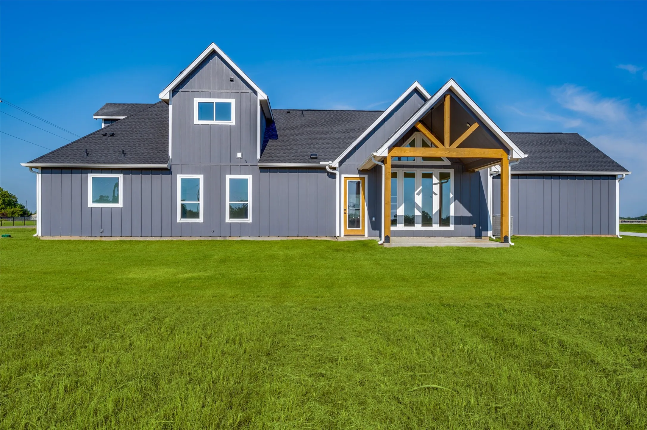 Contemporary farmhouse exterior with a covered patio featuring exposed timber framing, board and batten siding, multiple windows, and a dark shingle roof