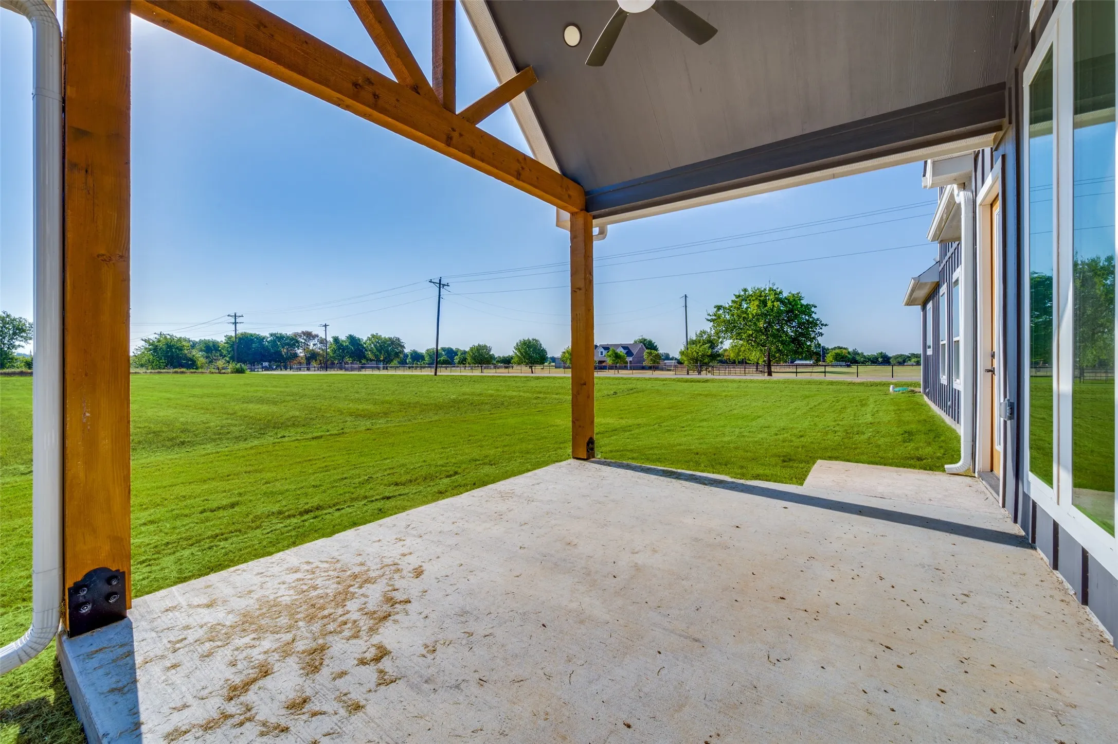 Covered concrete patio with exposed wood beam ceiling, equipped with a ceiling fan, and featuring a large grassy expanse