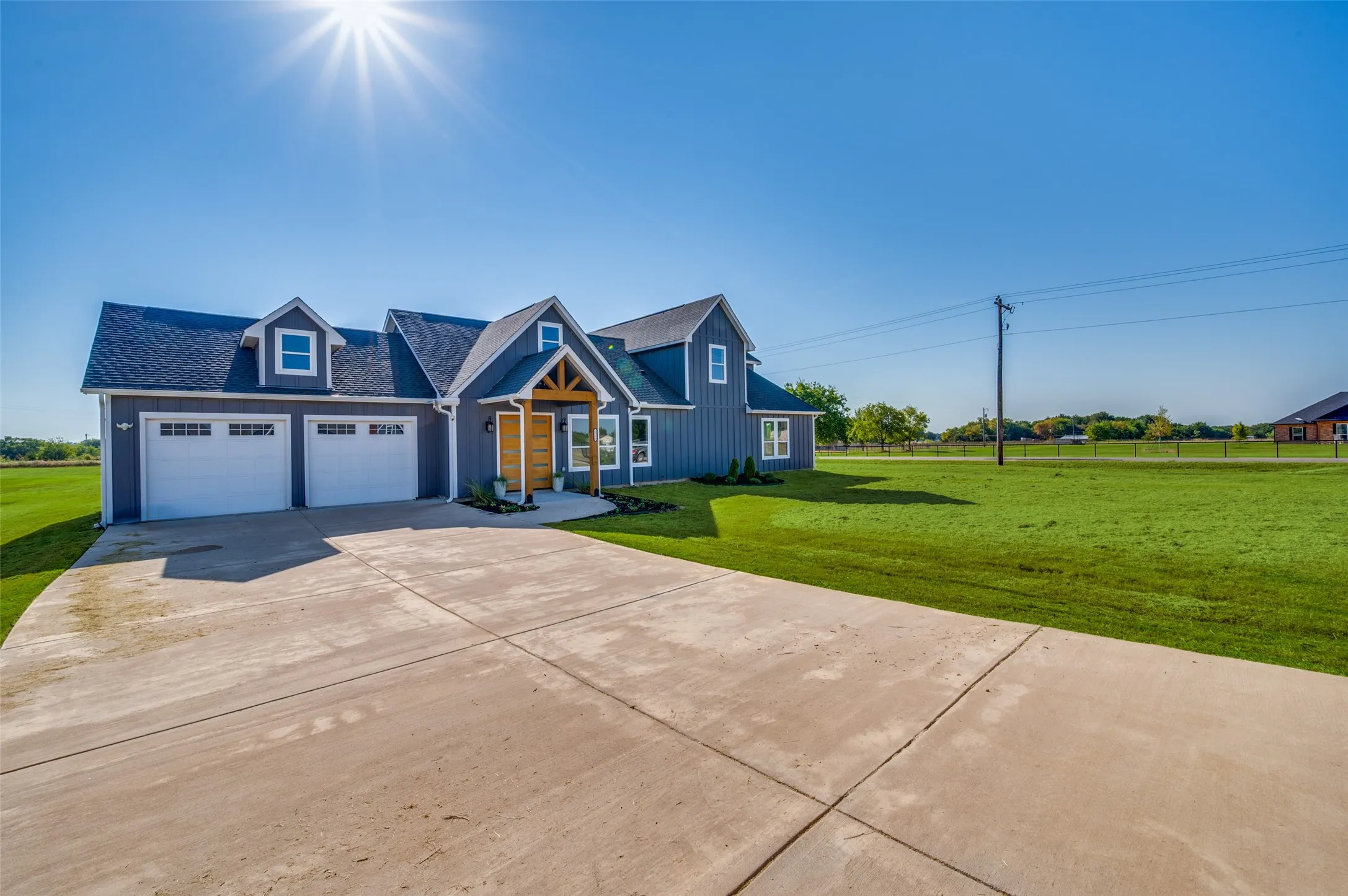 Modern farmhouse exterior with blue siding, a dark shingle roof, a two-car garage, and a concrete driveway