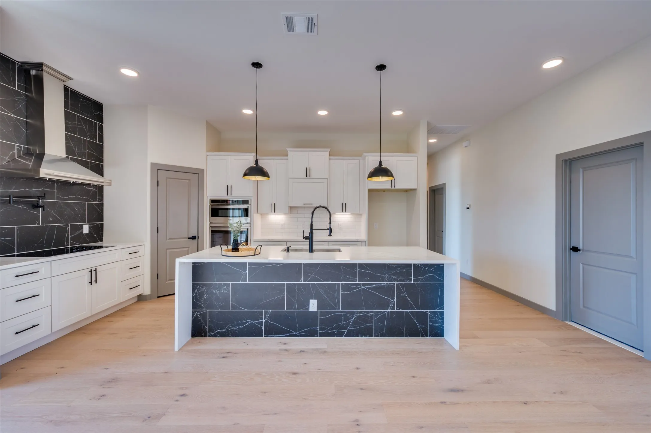 Modern kitchen featuring white cabinetry, black subway tile backsplash, a large kitchen island with pendant lighting, and wood-finish flooring