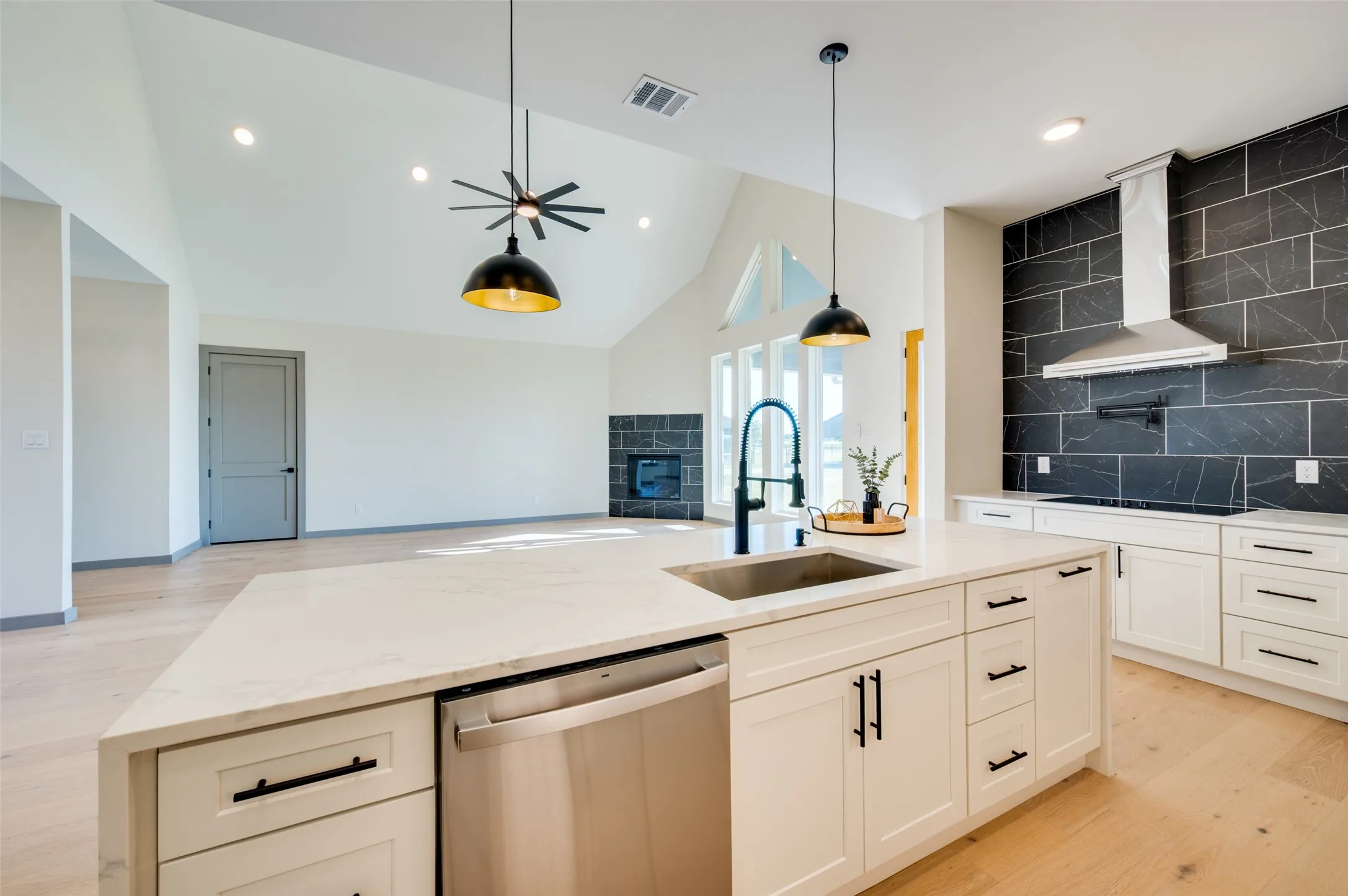 Gourmet kitchen featuring a large island with sink, white shaker cabinetry, stainless steel appliances, and a dark tile backsplash