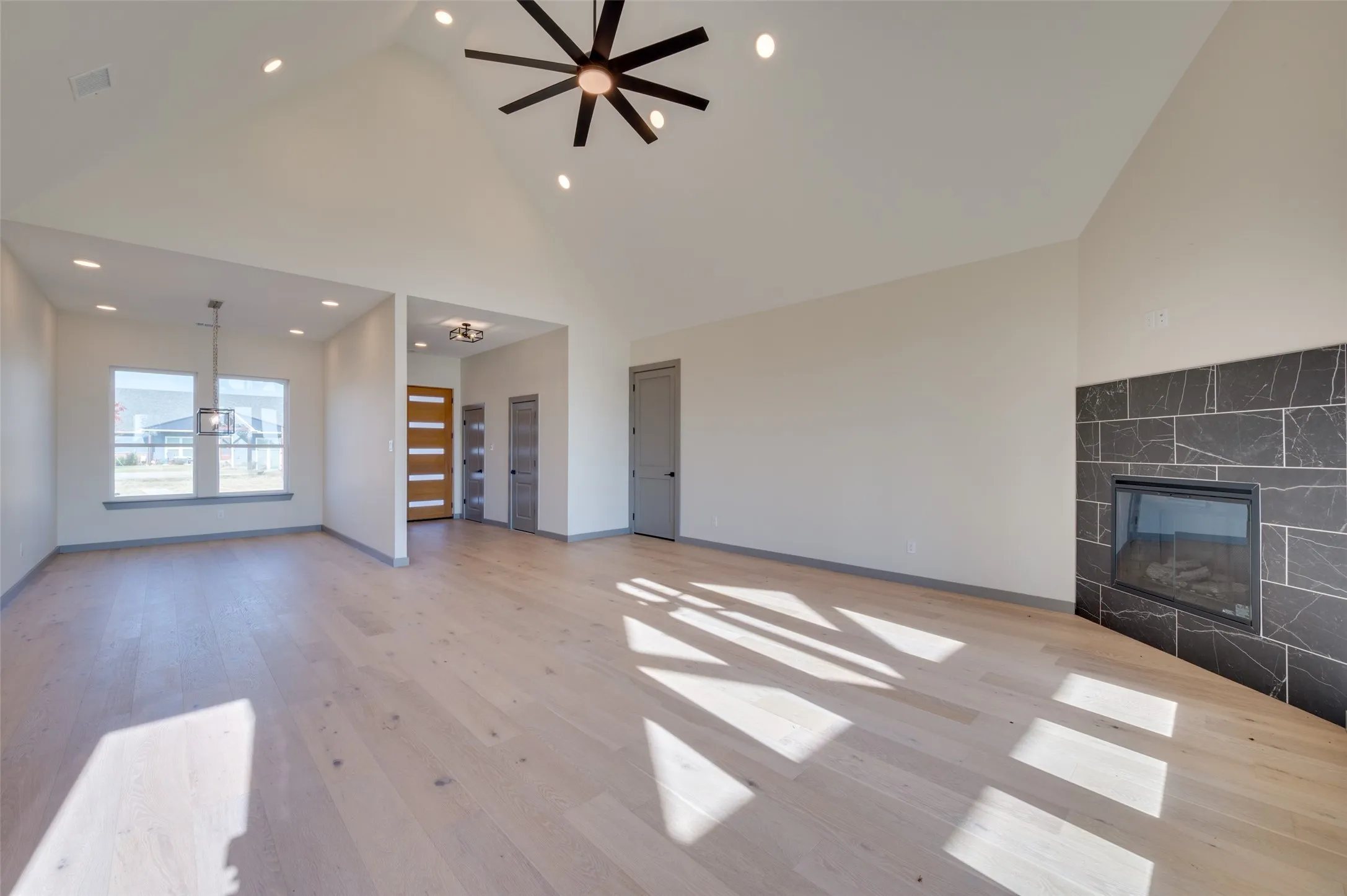 Vaulted ceilings with recessed lighting, wood-finish flooring, and a fireplace with a stone tile surround