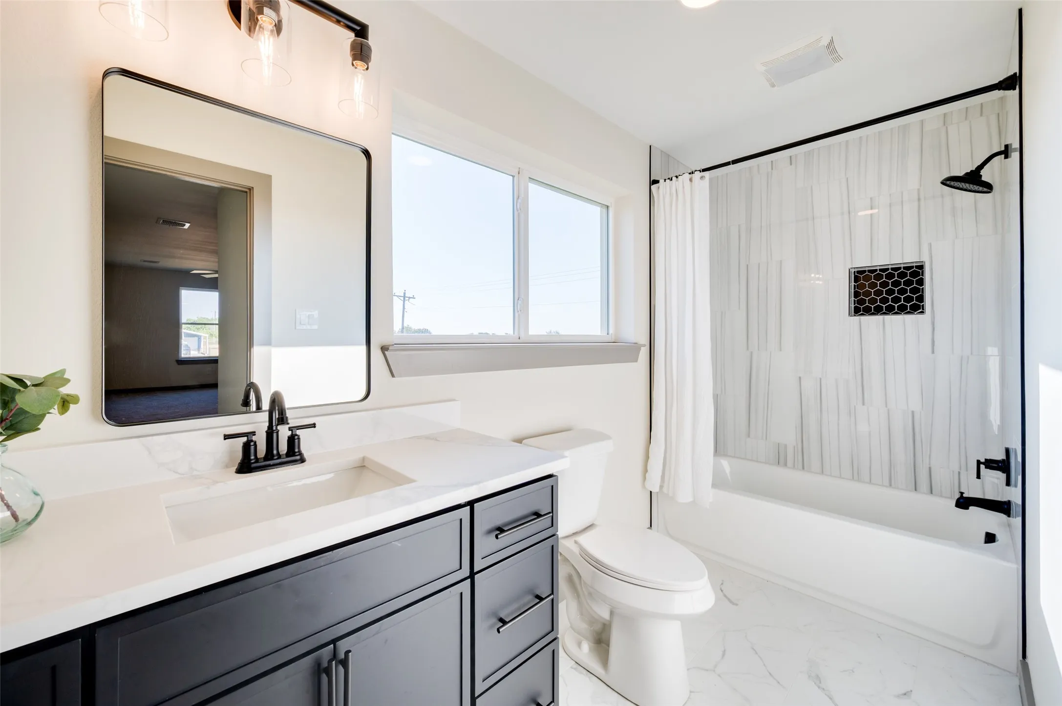 Vanity with solid surface countertop and integrated sink, black finish cabinetry, black finish fixtures, black frame mirror, and white tile flooring