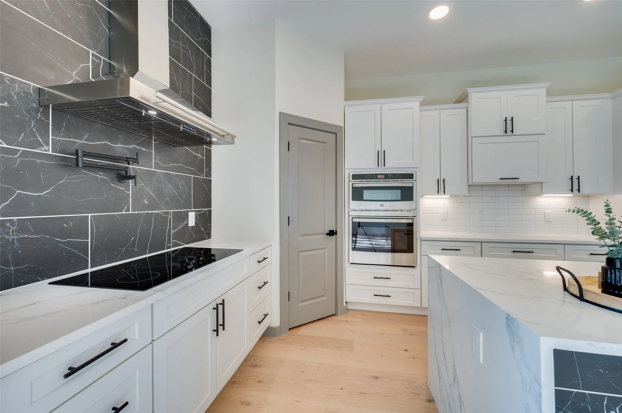 Modern kitchen featuring white shaker cabinetry, stainless steel appliances, a black electric cooktop, a dramatic black tiled backsplash, and a waterfall-edge island