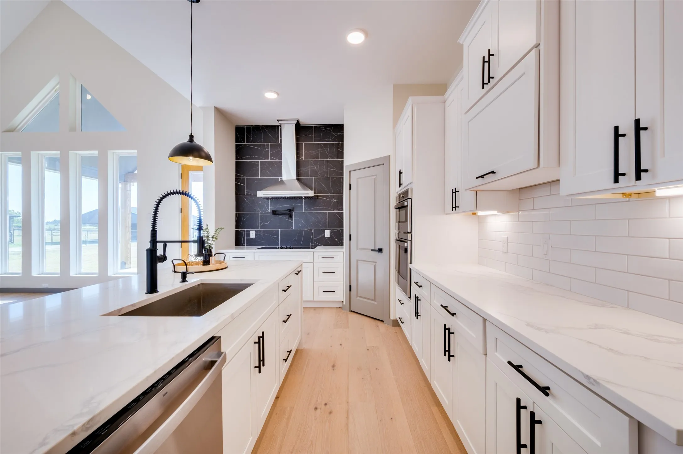 Kitchen featuring a large island with an undermount sink, white cabinetry with black hardware, stone countertops, and a full-height tile backsplash