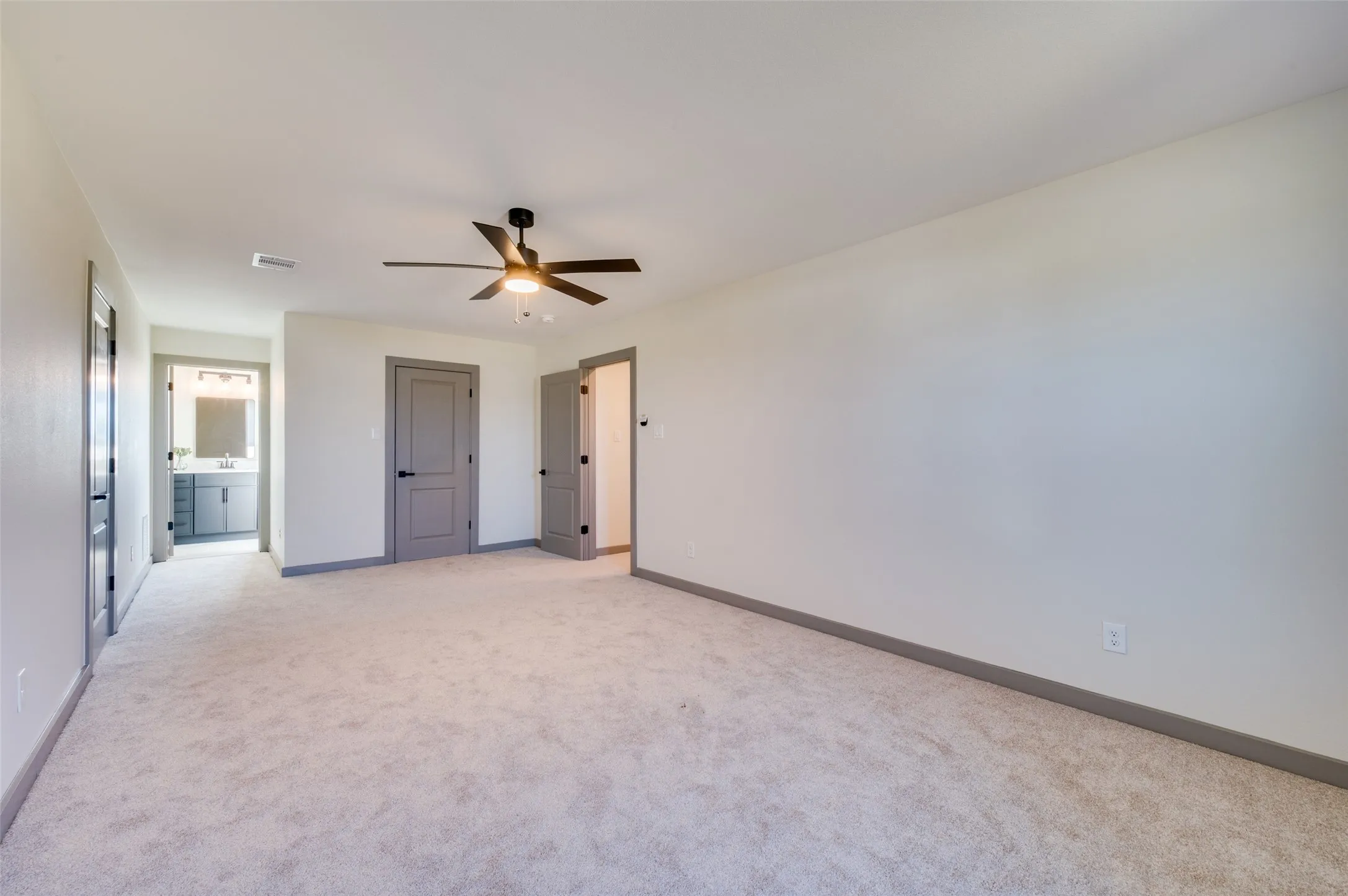 Spacious room with light-colored carpeting, a ceiling fan with integrated lighting, and multiple interior doors