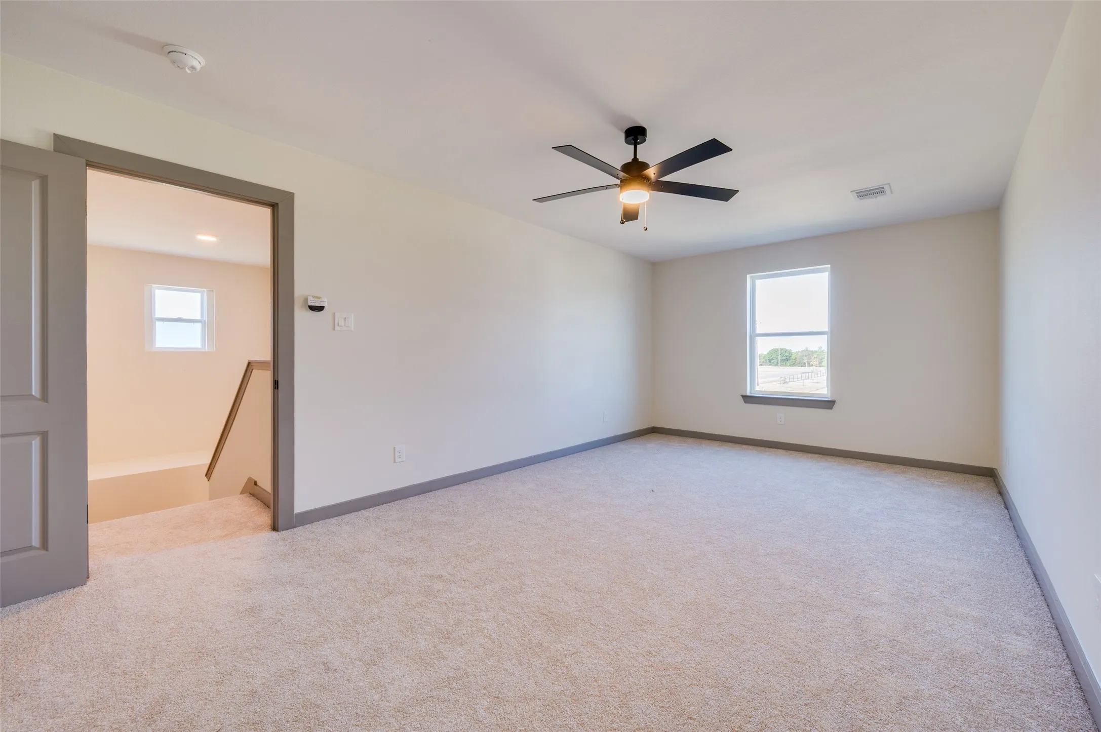 Spacious room with plush carpeting, neutral wall finishes, a modern ceiling fan, and a large window