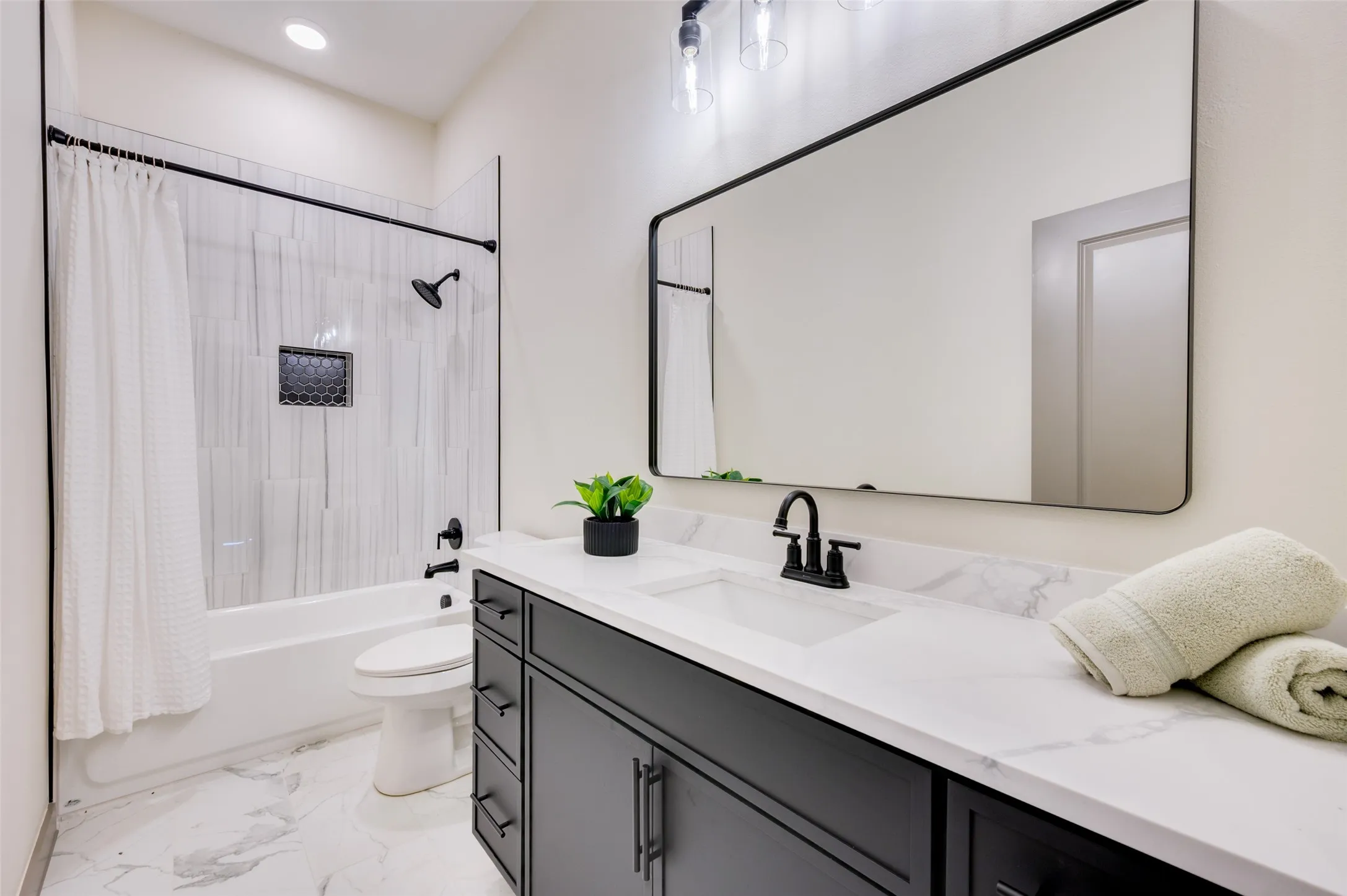Integrated bathtub with shower, vanity with dual sinks, black-framed mirror, and marble-finish flooring