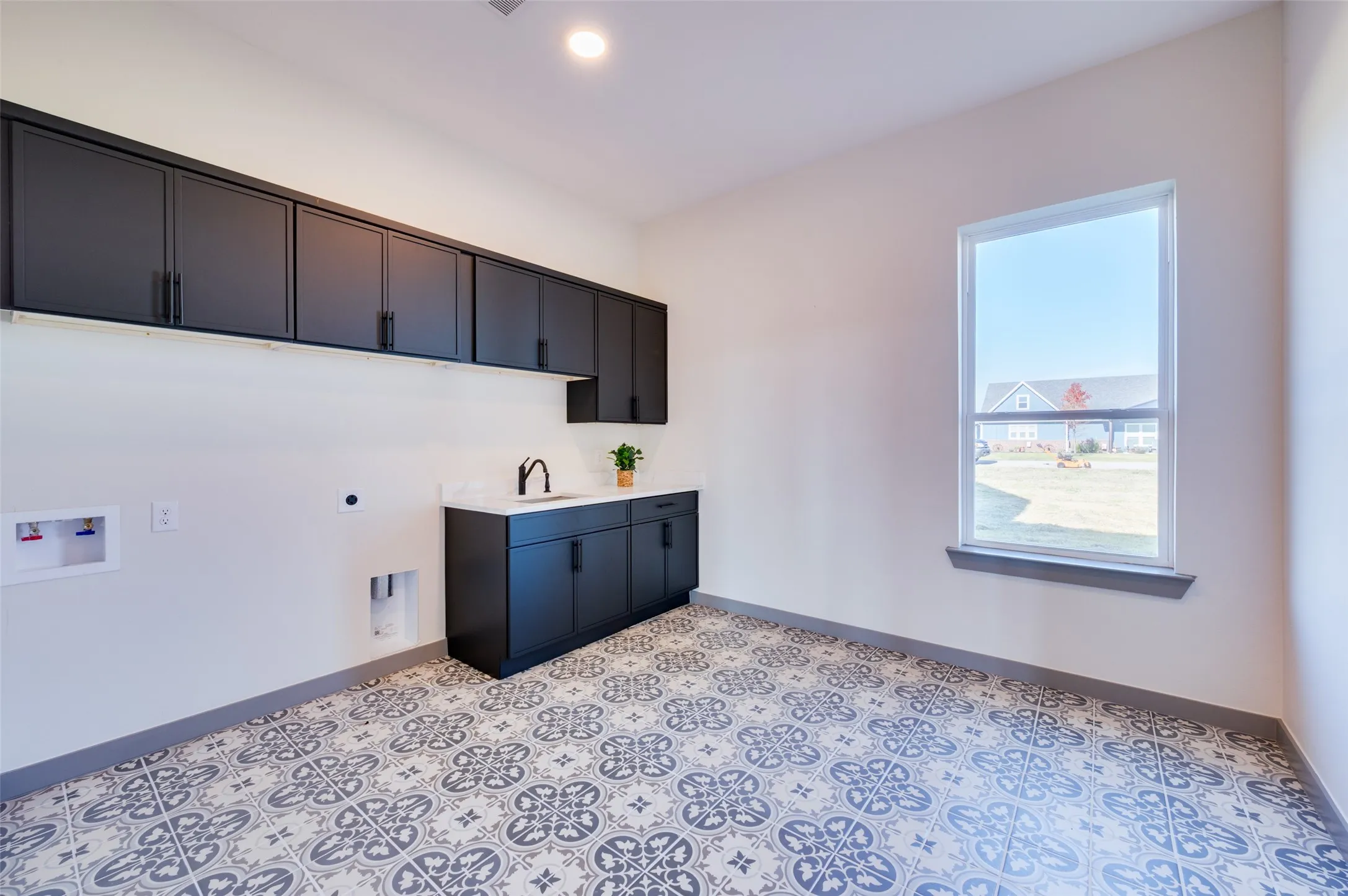 Patterned floor tiles, built-in cabinetry, countertop with sink, wall-mounted faucet, and a window