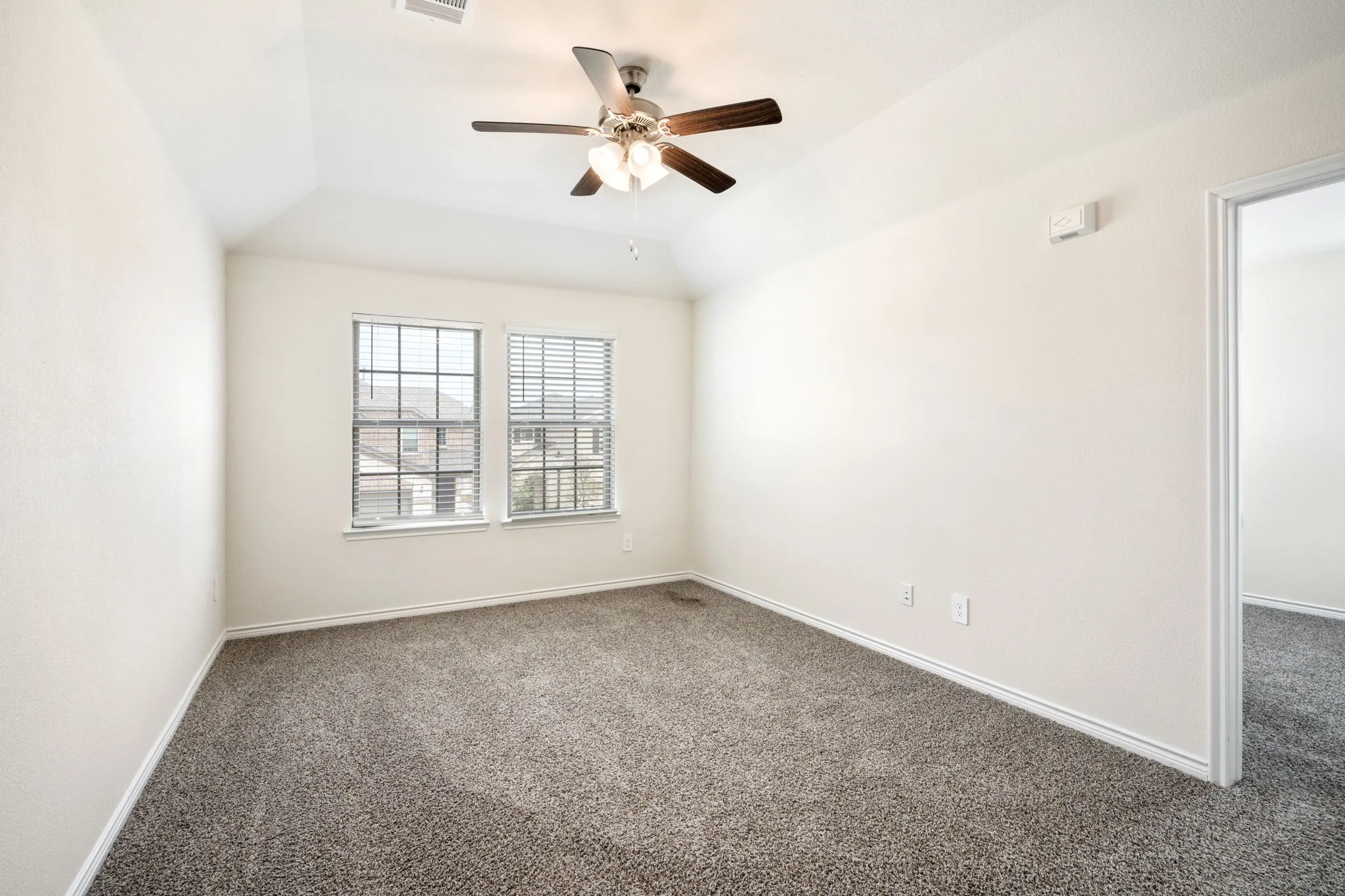 Vaulted ceiling with an attached ceiling fan, dual windows with blinds, and neutral carpet flooring