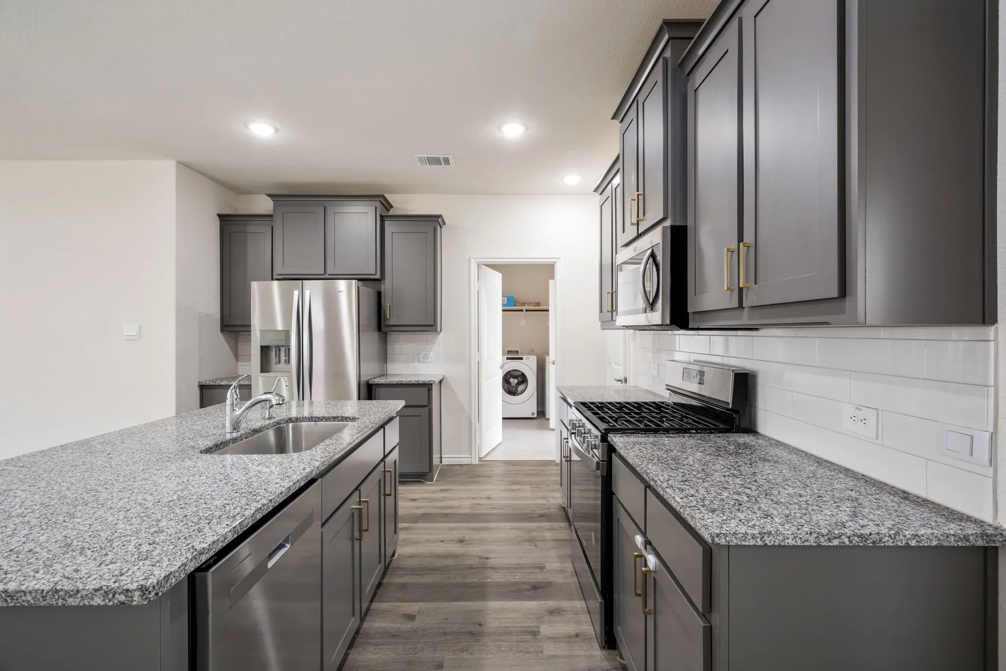Kitchen featuring dark cabinetry, speckled countertops, stainless steel appliances, a white subway tile backsplash, and wood-finish flooring