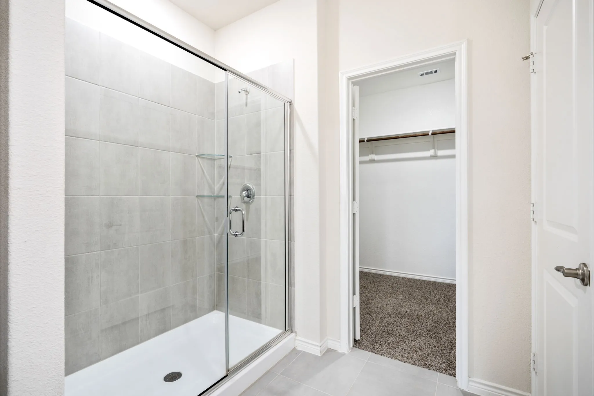 Enclosed shower with clear glass door, chrome fixtures, and integrated shelving
