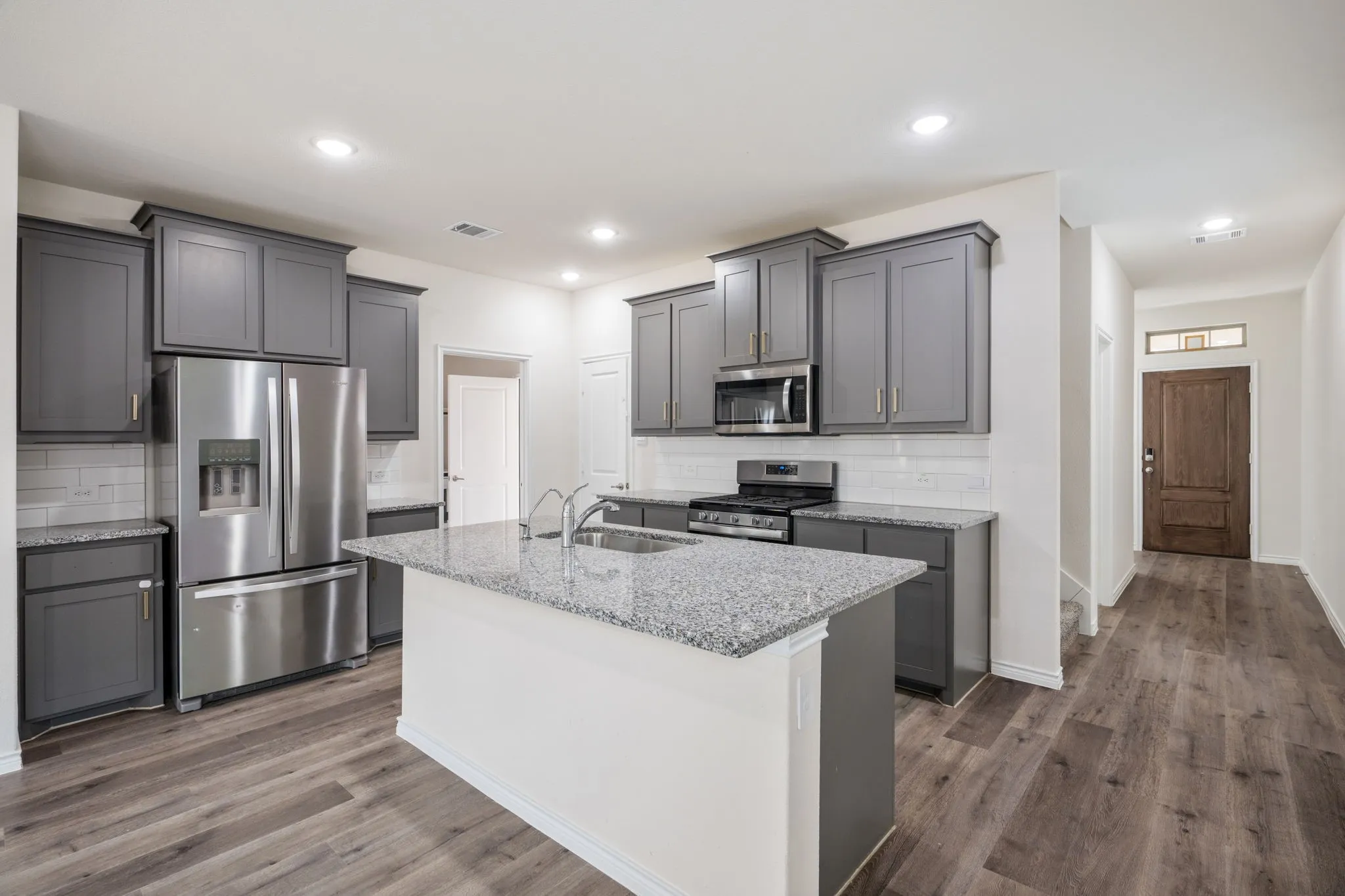 Kitchen featuring stainless steel appliances, white subway tile backsplash, granite countertops, and wood-finish flooring