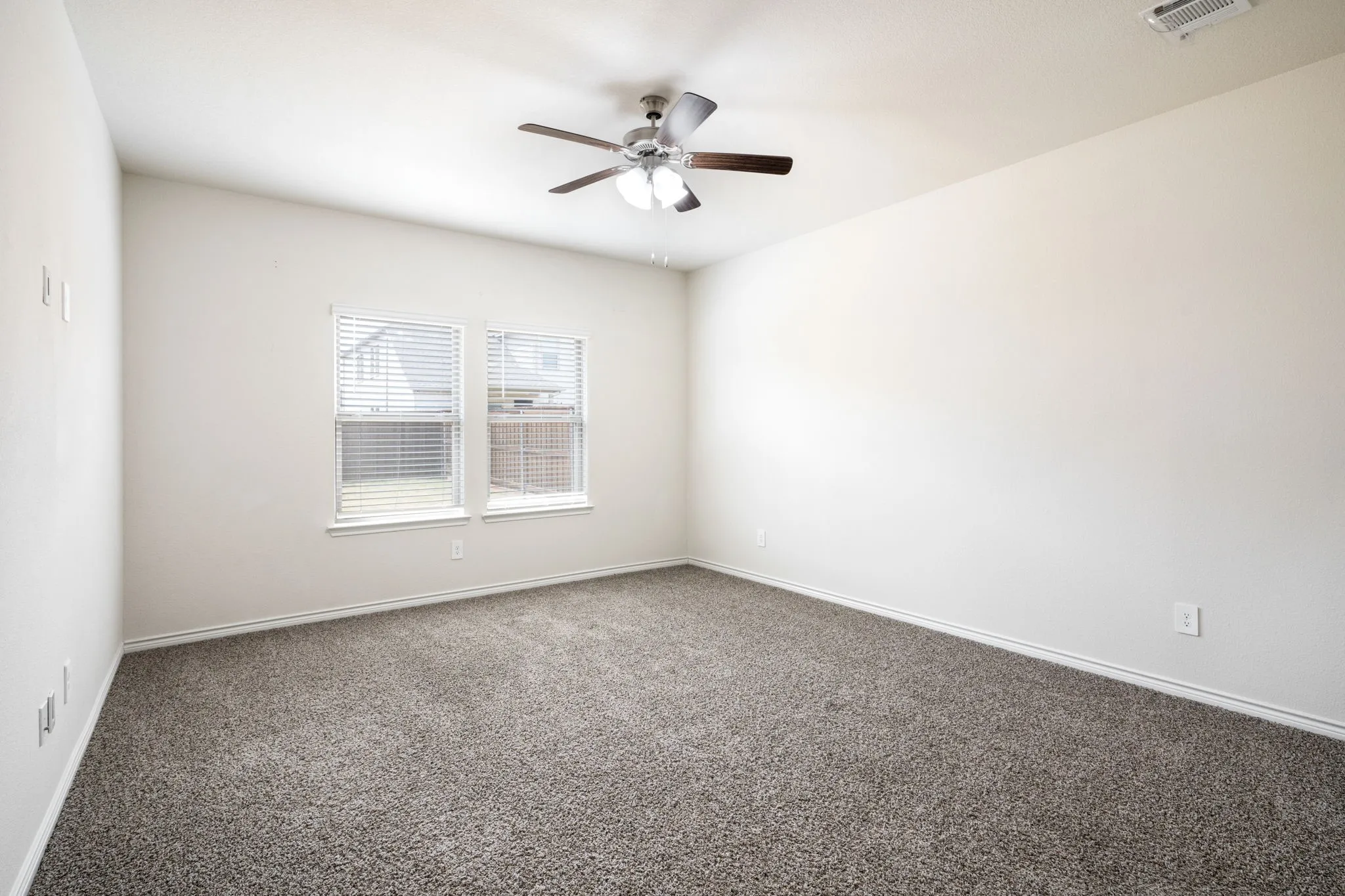 Recessed dual windows with horizontal blinds, overhead ceiling fan with integrated lighting, and neutral carpeting