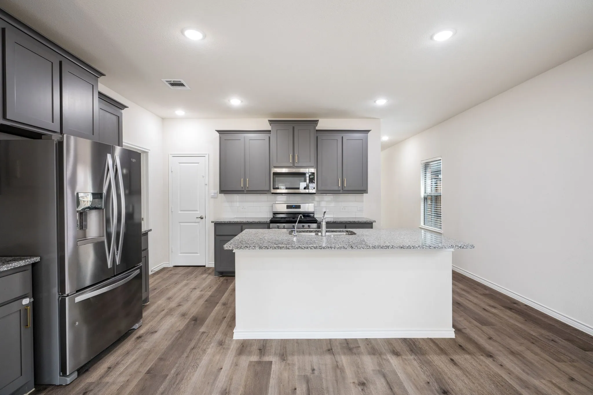 Kitchen featuring a center island, stainless steel appliances, grey cabinetry, wood-finish flooring, and recessed lighting