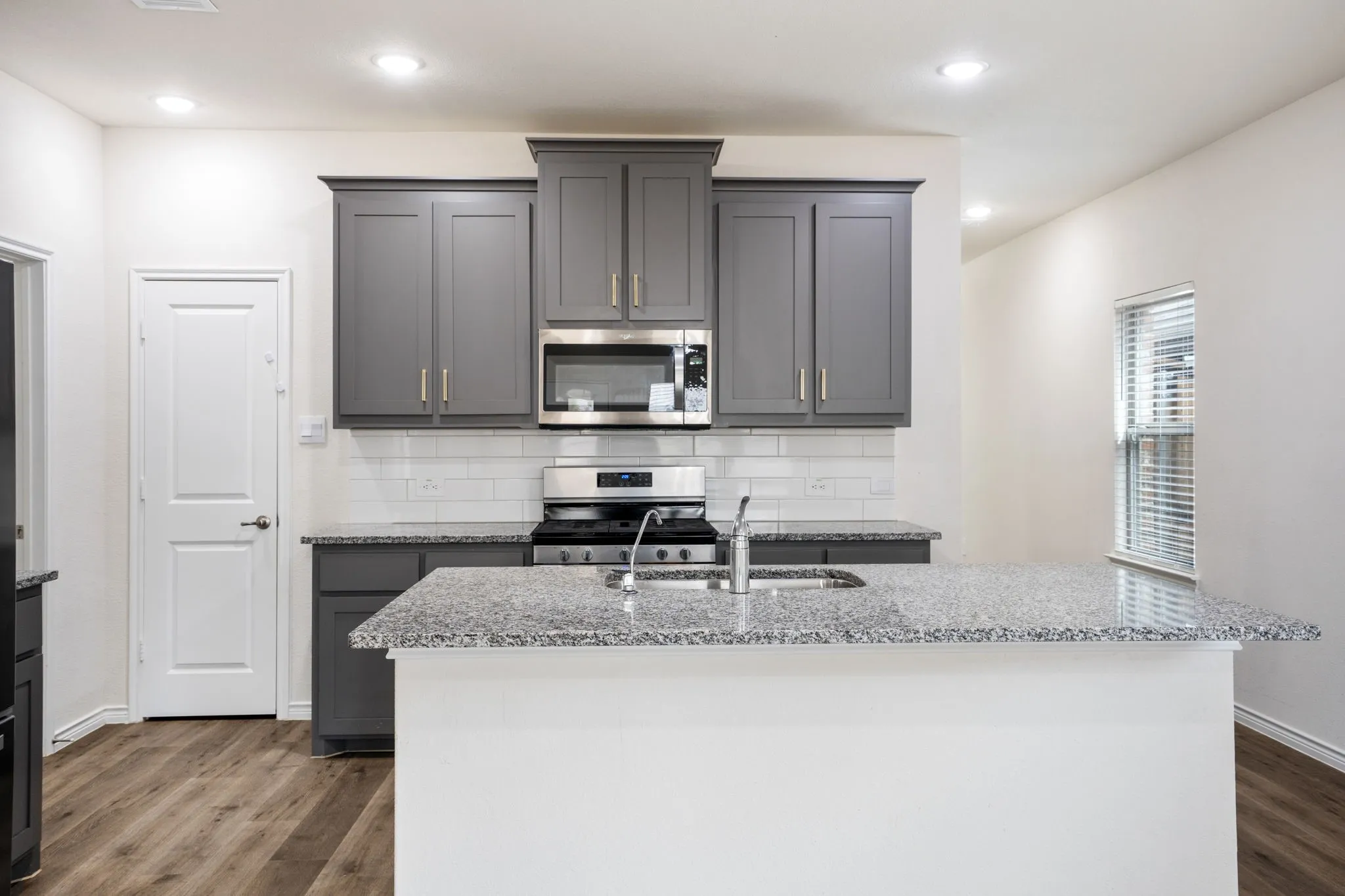 Kitchen featuring wood-finish flooring, gray cabinetry, stainless steel appliances, a tile backsplash, and light-toned countertops