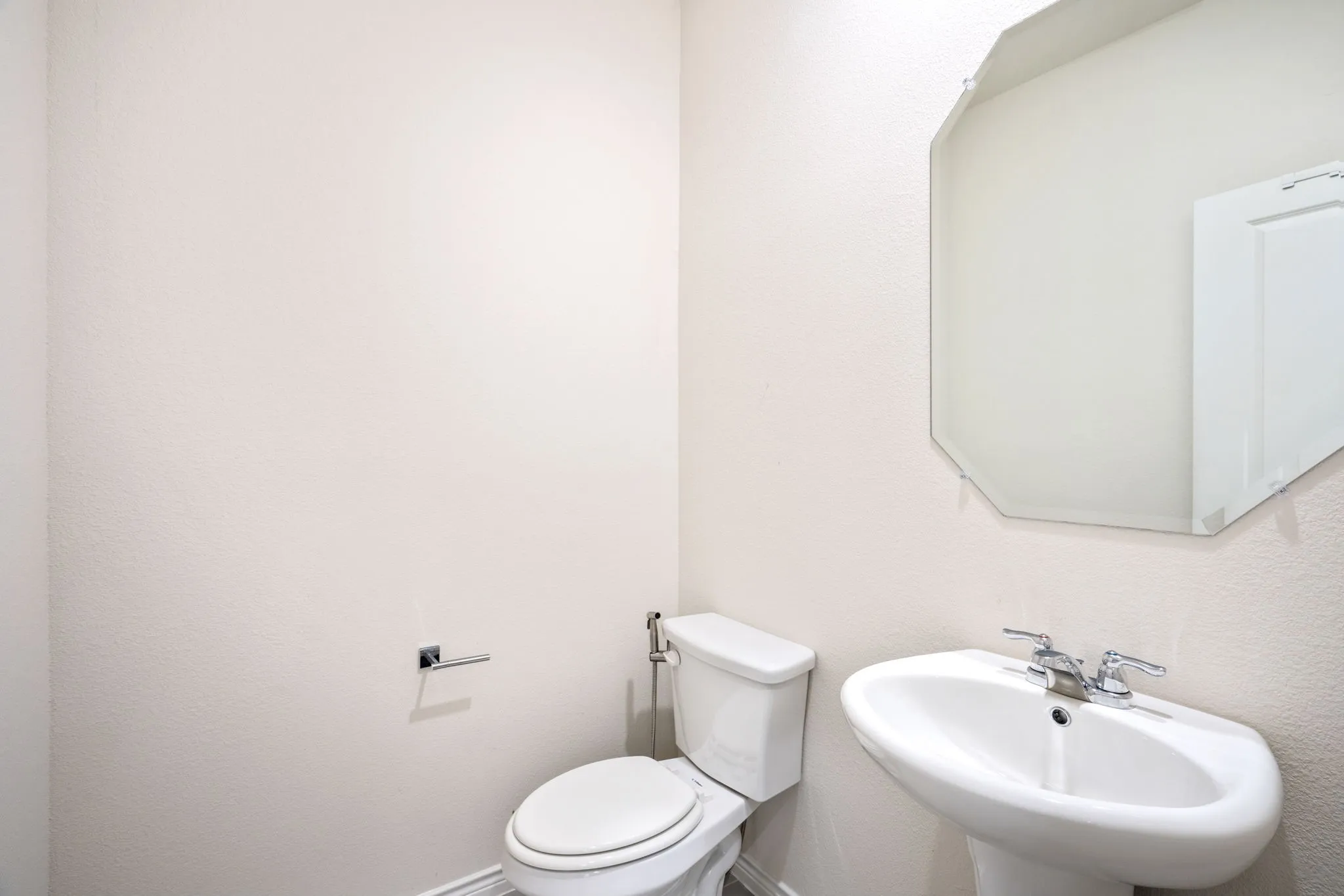 Pedestal sink with chrome faucet, octagonal mirror, and white toilet