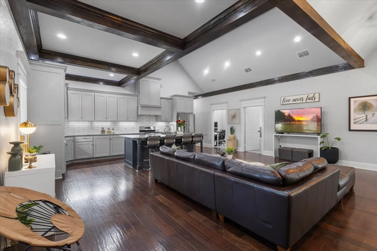 Vaulted ceiling with dark wood-finish beams, recessed lighting, wood-finish flooring, light grey cabinetry, and a kitchen island with seating