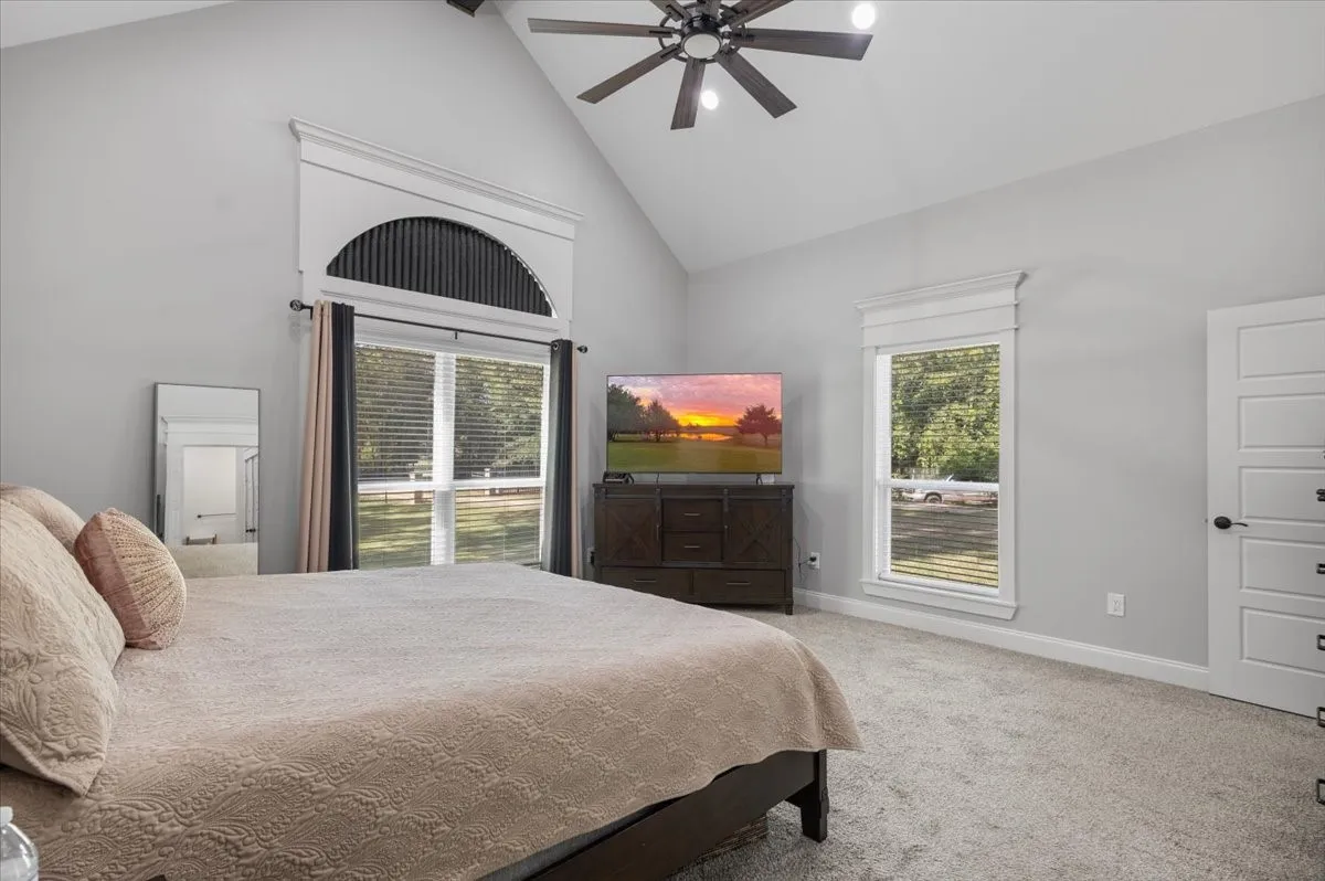 Vaulted ceiling with a ceiling fan, carpeted flooring, and multiple windows with trim