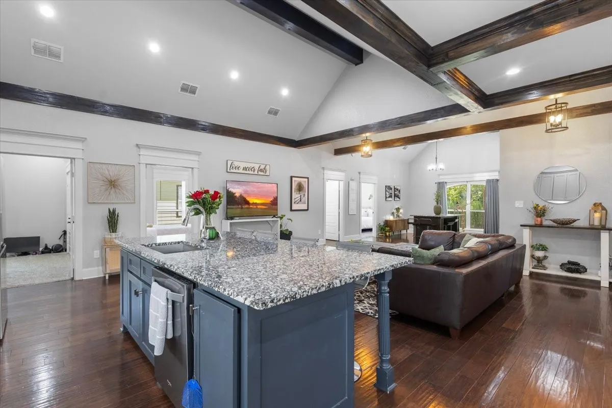 Open-concept living space with vaulted ceilings, exposed wood beams, wood-finish flooring, a kitchen island with stone countertops, and recessed lighting