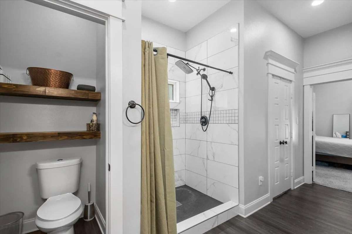 Walk-in shower with large format wall tiles and mosaic accent, dark flooring, and a floating wood shelf storage