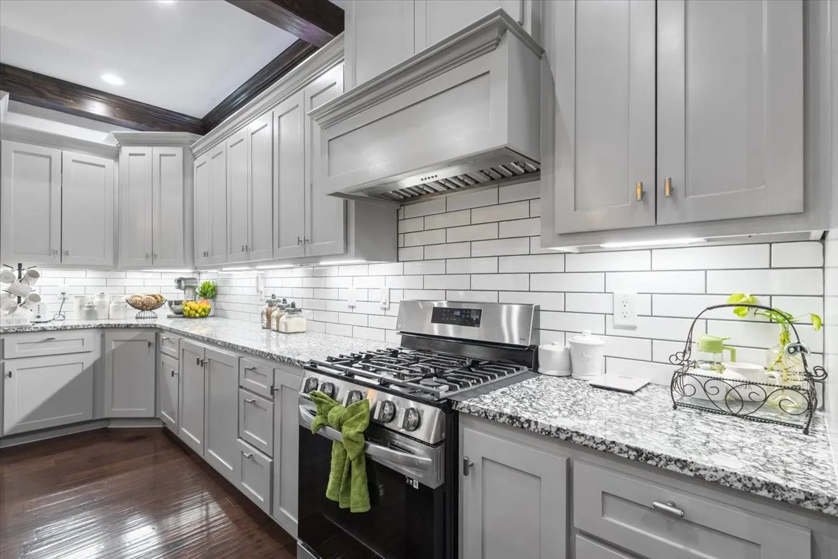 Light gray cabinetry with gold-tone hardware, granite-style countertops, subway tile backsplash, and wood-finish flooring