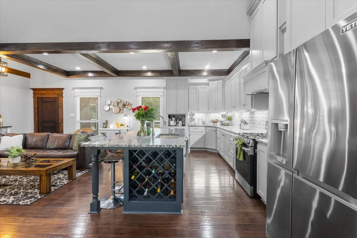 Hardwood-finish flooring, coffered ceiling with recessed lighting, kitchen island with built-in wine storage, stainless steel refrigerator, and white cabinetry