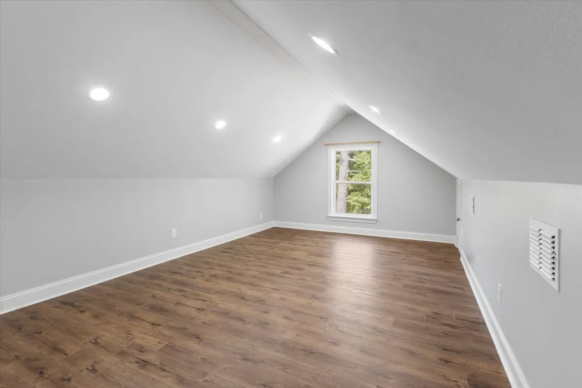 Bright attic space with sloped ceilings, wood-finish flooring, recessed lighting, and a prominent window
