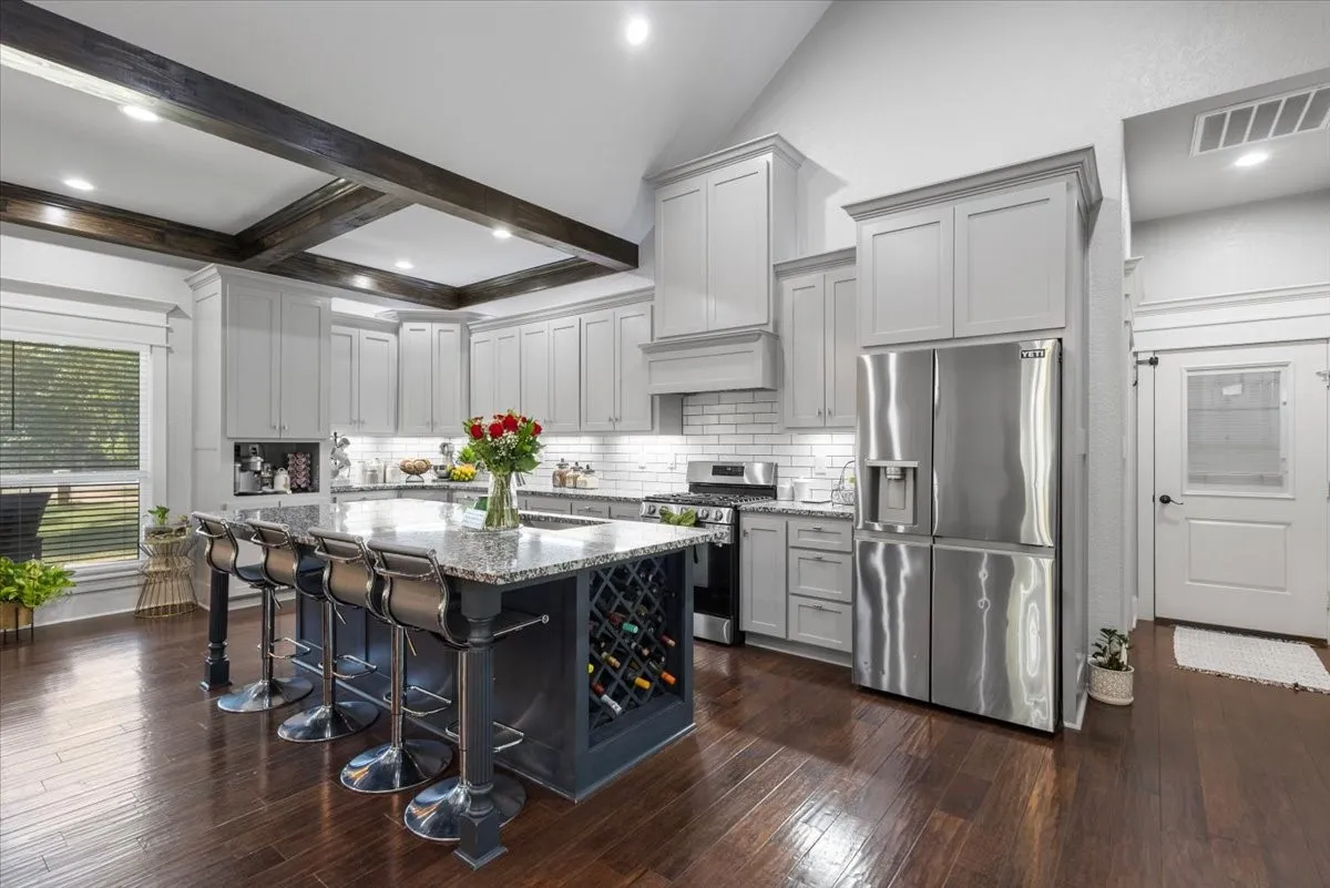 Vaulted ceiling with exposed wood beams, stainless steel appliances, wood-finish flooring, white subway tile backsplash, and an island with built-in wine storage