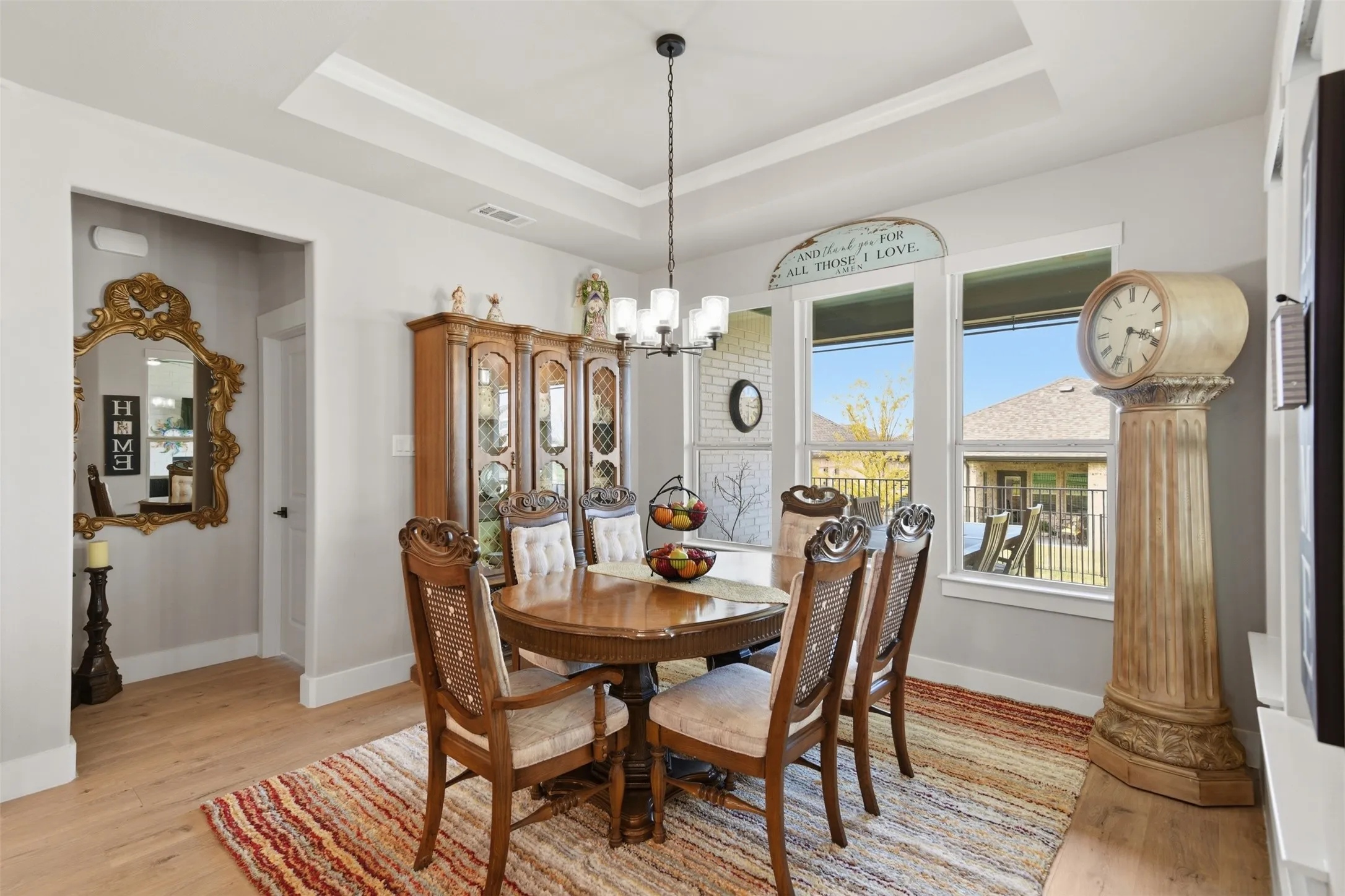 Tray ceiling with crown molding, chandelier lighting, wood-finish flooring, multiple windows, and a doorway with trim
