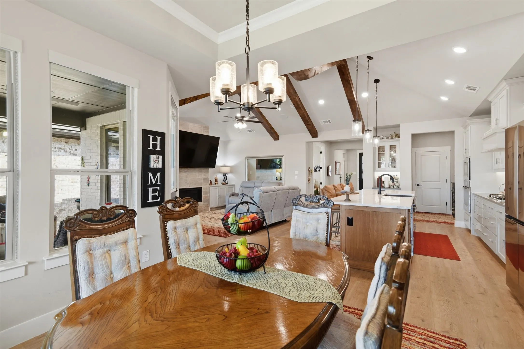 Vaulted ceilings with exposed wood beams, wood-finish flooring, a kitchen island with pendant lighting, a built-in fireplace, and a covered outdoor patio