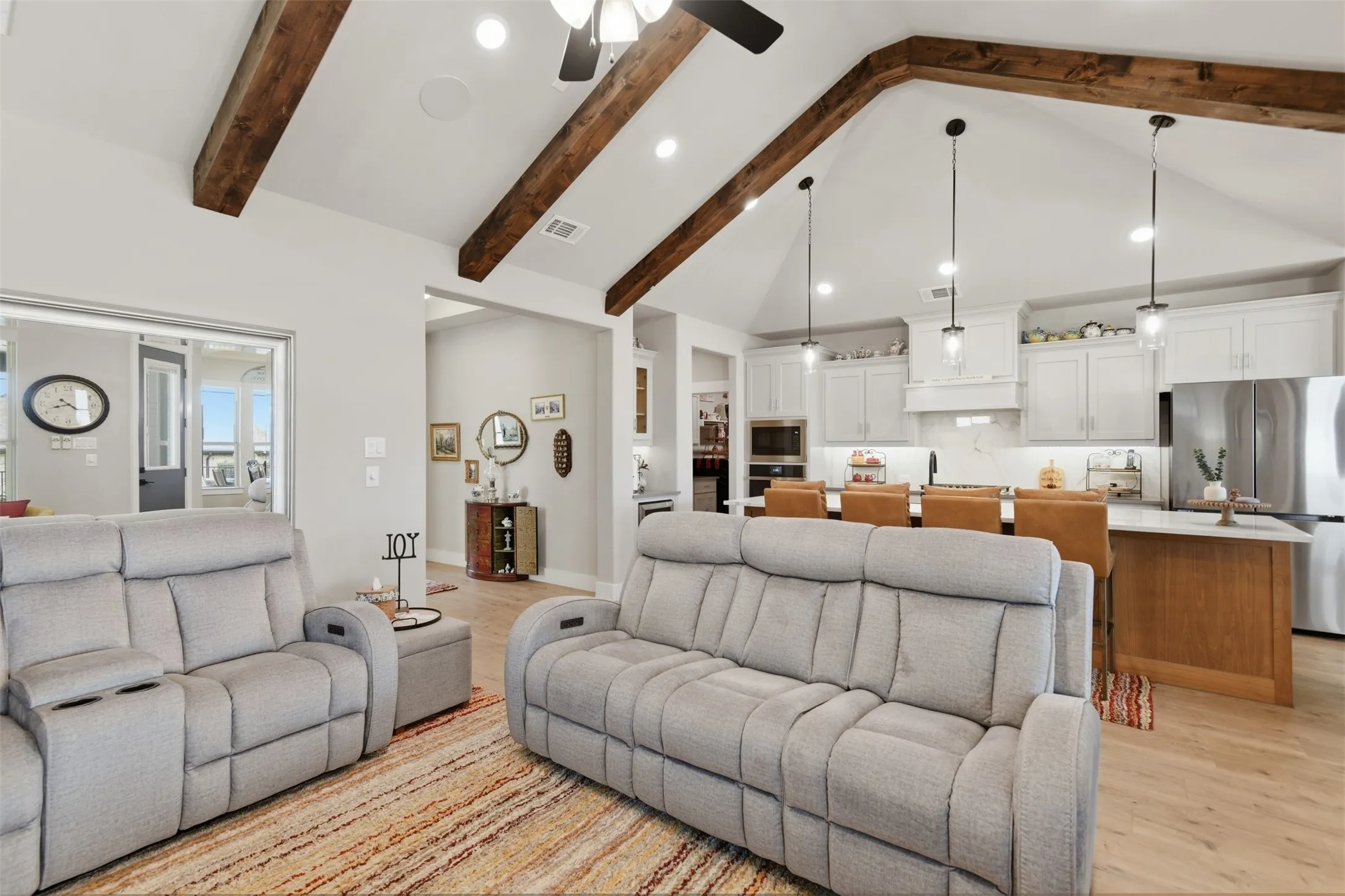 Vaulted ceiling with exposed wood beams, recessed lighting, wood-finish flooring, white cabinetry, and stainless steel appliances