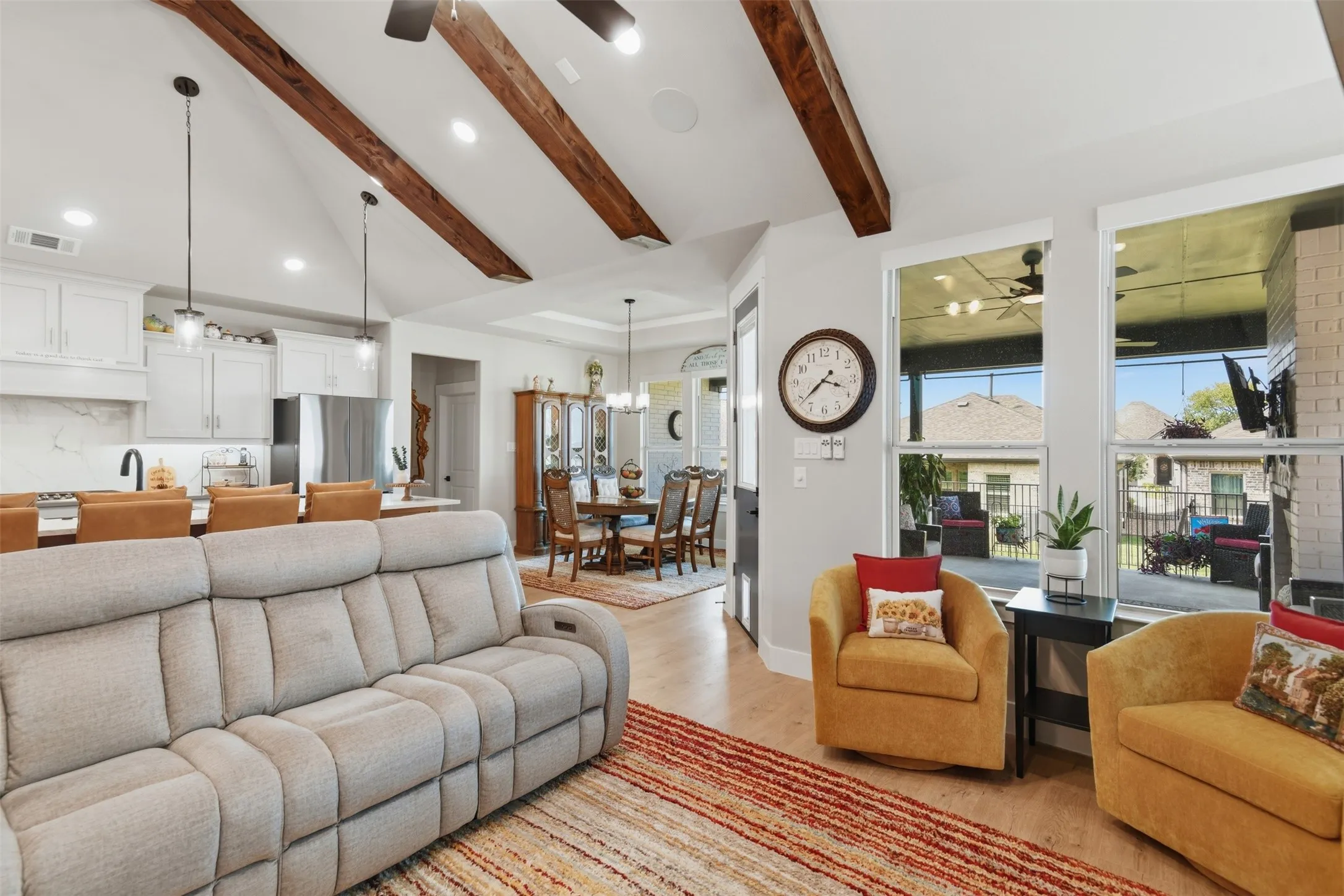 Vaulted ceilings with exposed wood beams, wood-finish flooring, white cabinetry, a screened patio, and a brick fireplace