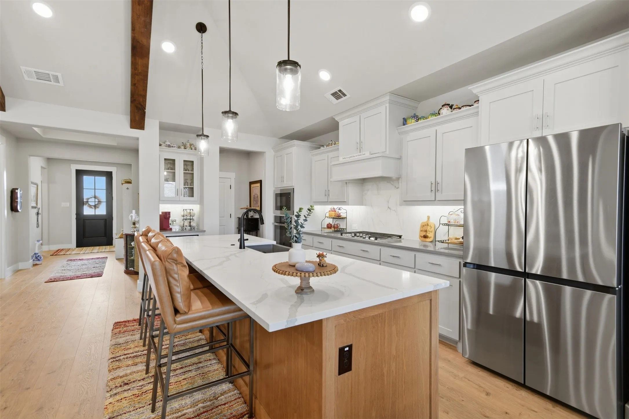 Spacious kitchen featuring an extended island, white cabinetry, integrated stainless steel appliances, wood-finish flooring, and exposed ceiling beams
