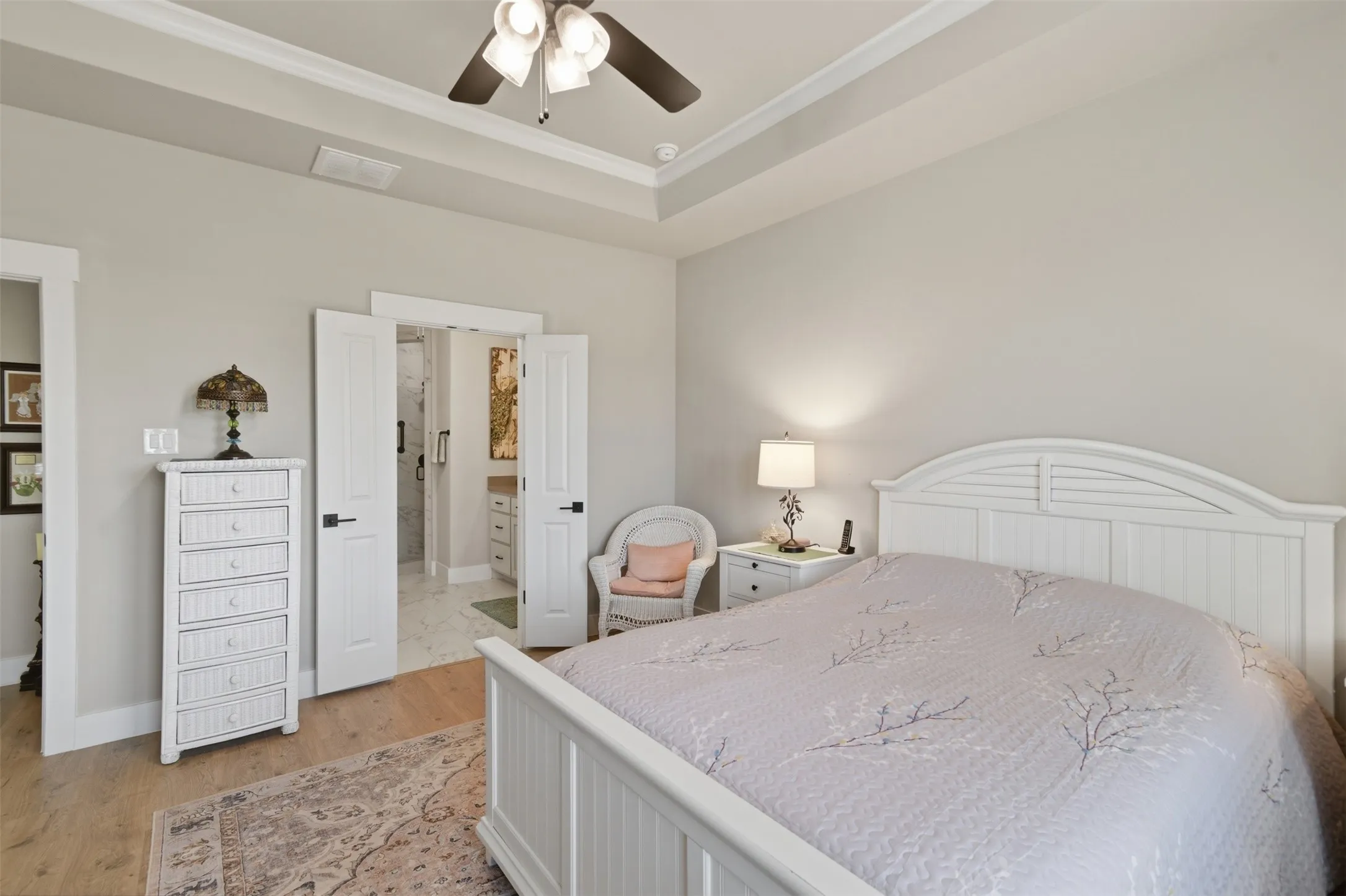 Tray ceiling with crown molding, wood-finish flooring, white paneled doors, and a ceiling fan with integrated lighting