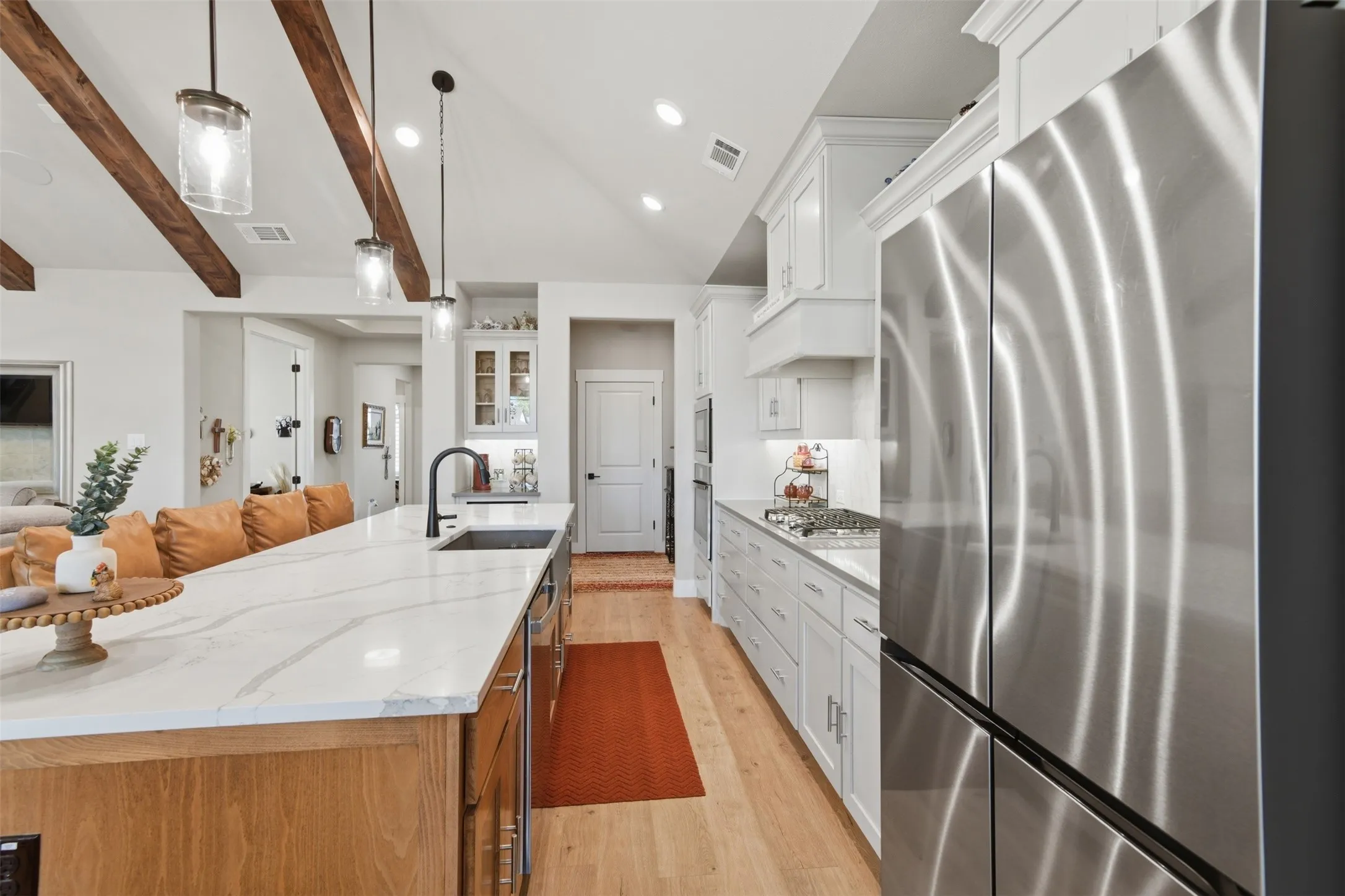 Vaulted ceiling with exposed wood beams, large kitchen island with a light-toned countertop, stainless steel appliances, white cabinetry, and wood-finish flooring