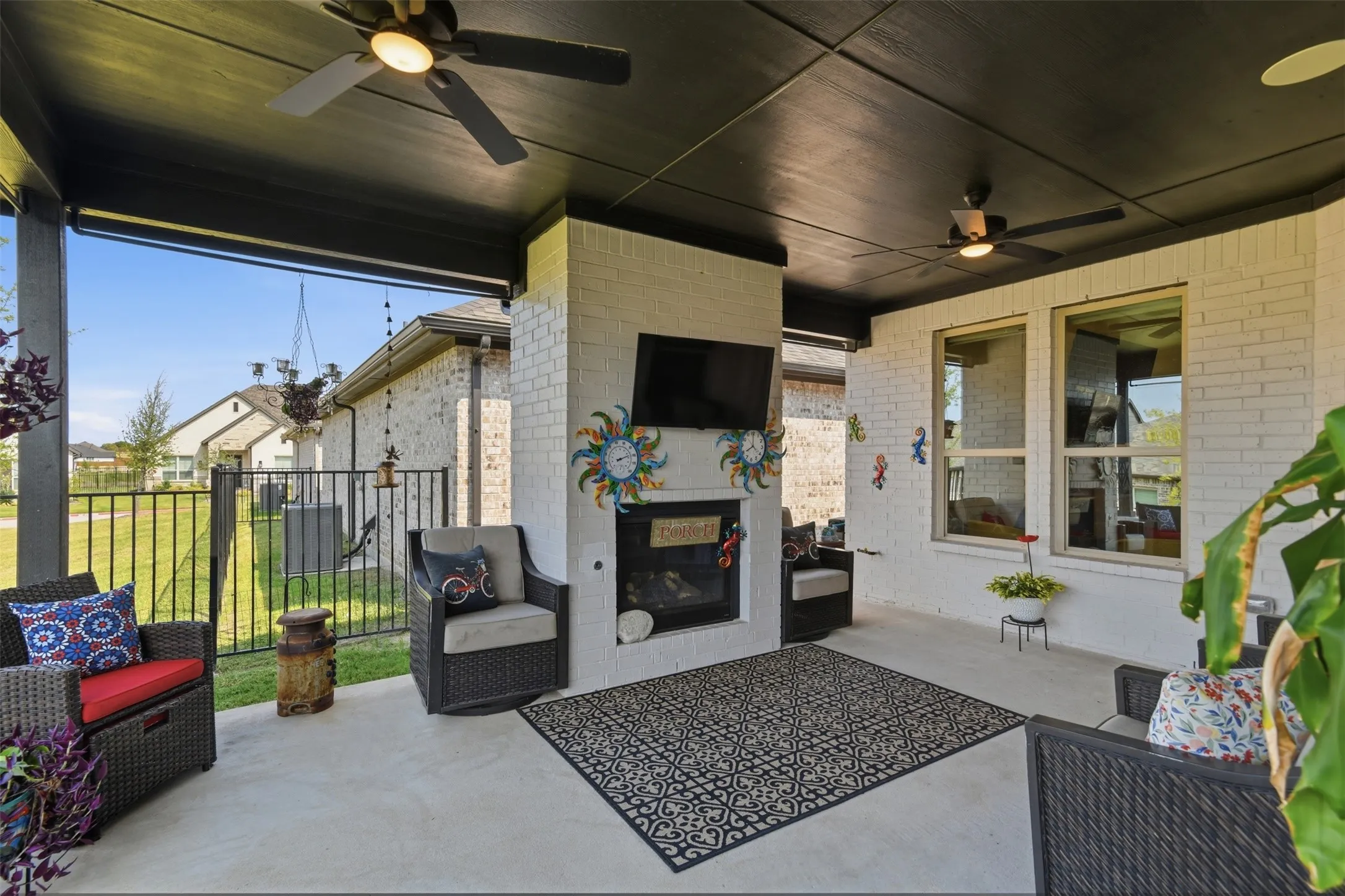 Covered patio featuring a painted brick fireplace, a ceiling fan, and concrete flooring
