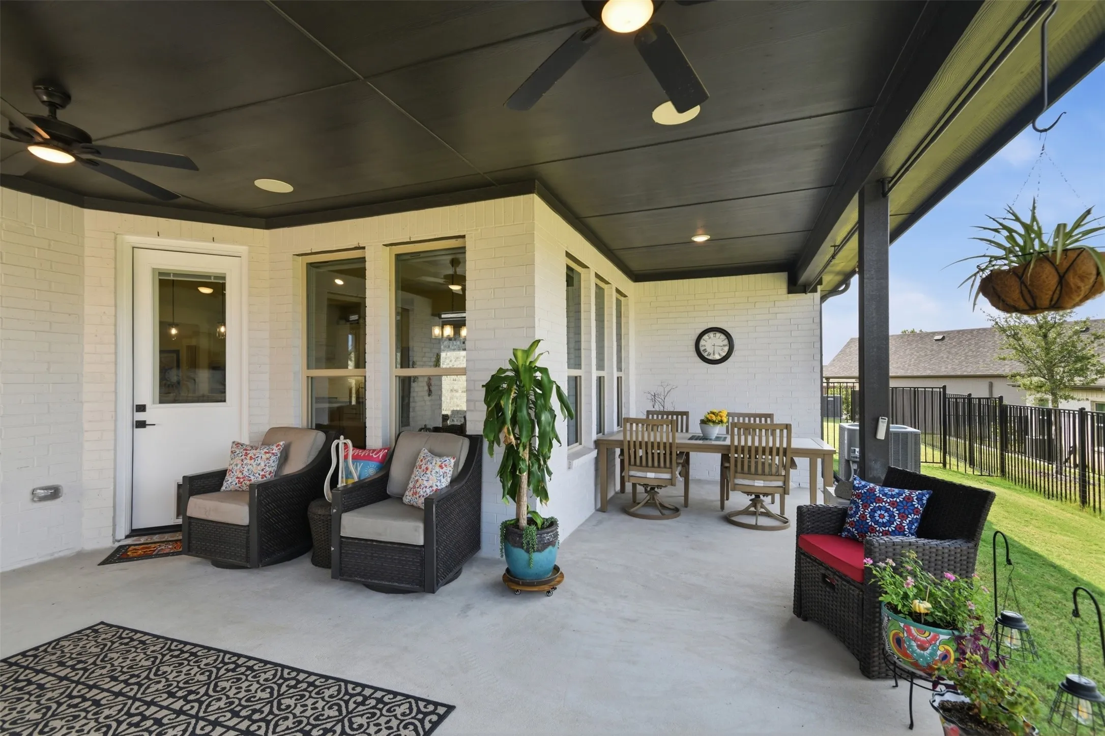 Expansive covered patio featuring a concrete surface, white brick exterior, black ceiling fans, recessed lighting, and a black wrought iron fence