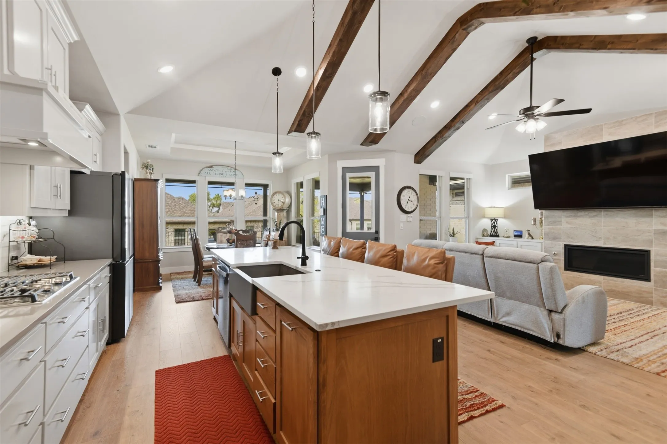 Kitchen island with countertop seating, wood-finish flooring, vaulted ceiling with exposed beams, fireplace with tile surround, and recessed lighting