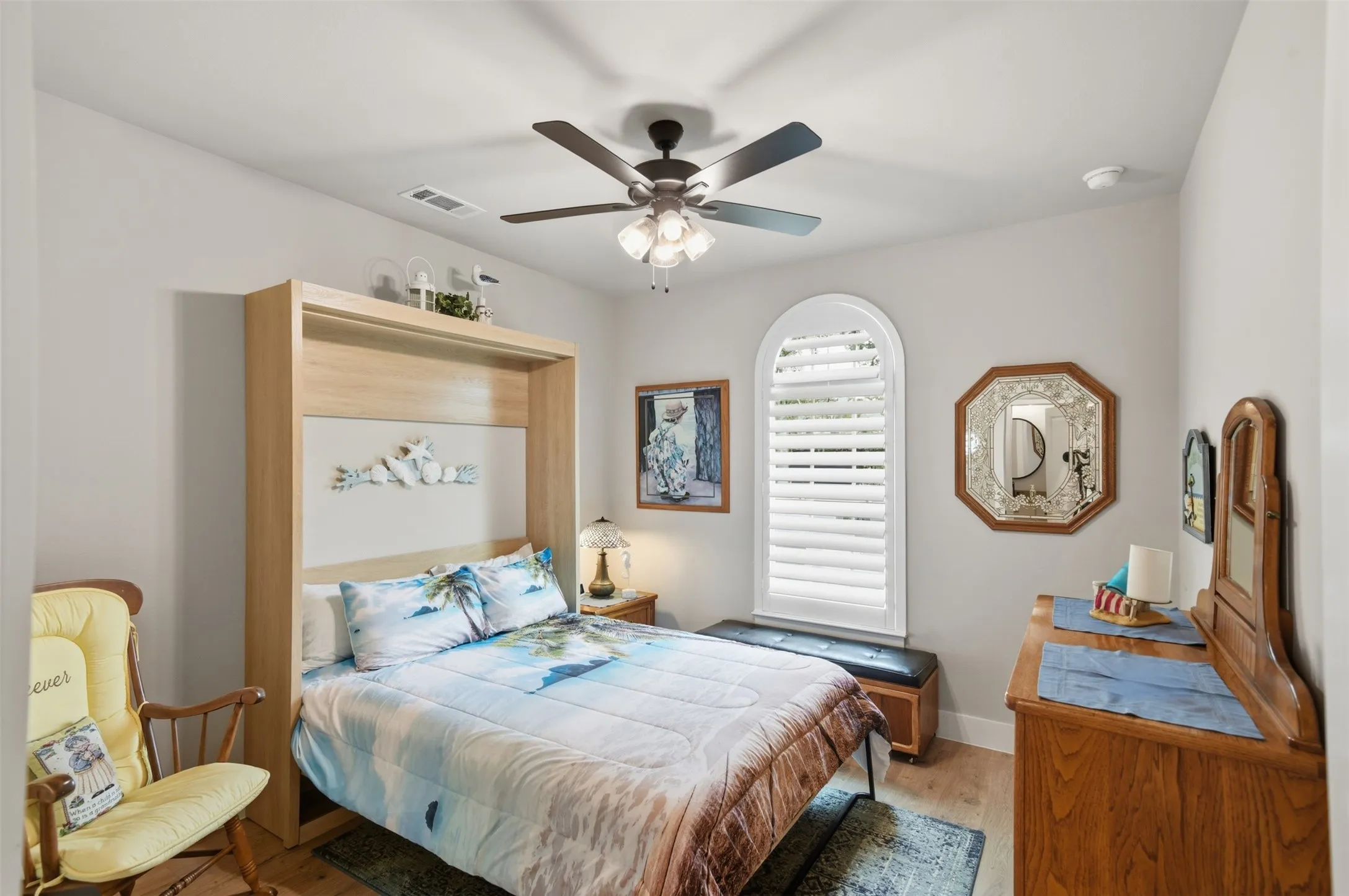 Built-in Murphy bed, arched window with plantation shutters, ceiling fan with integrated lighting, wood-finish flooring, and light-toned wall paint