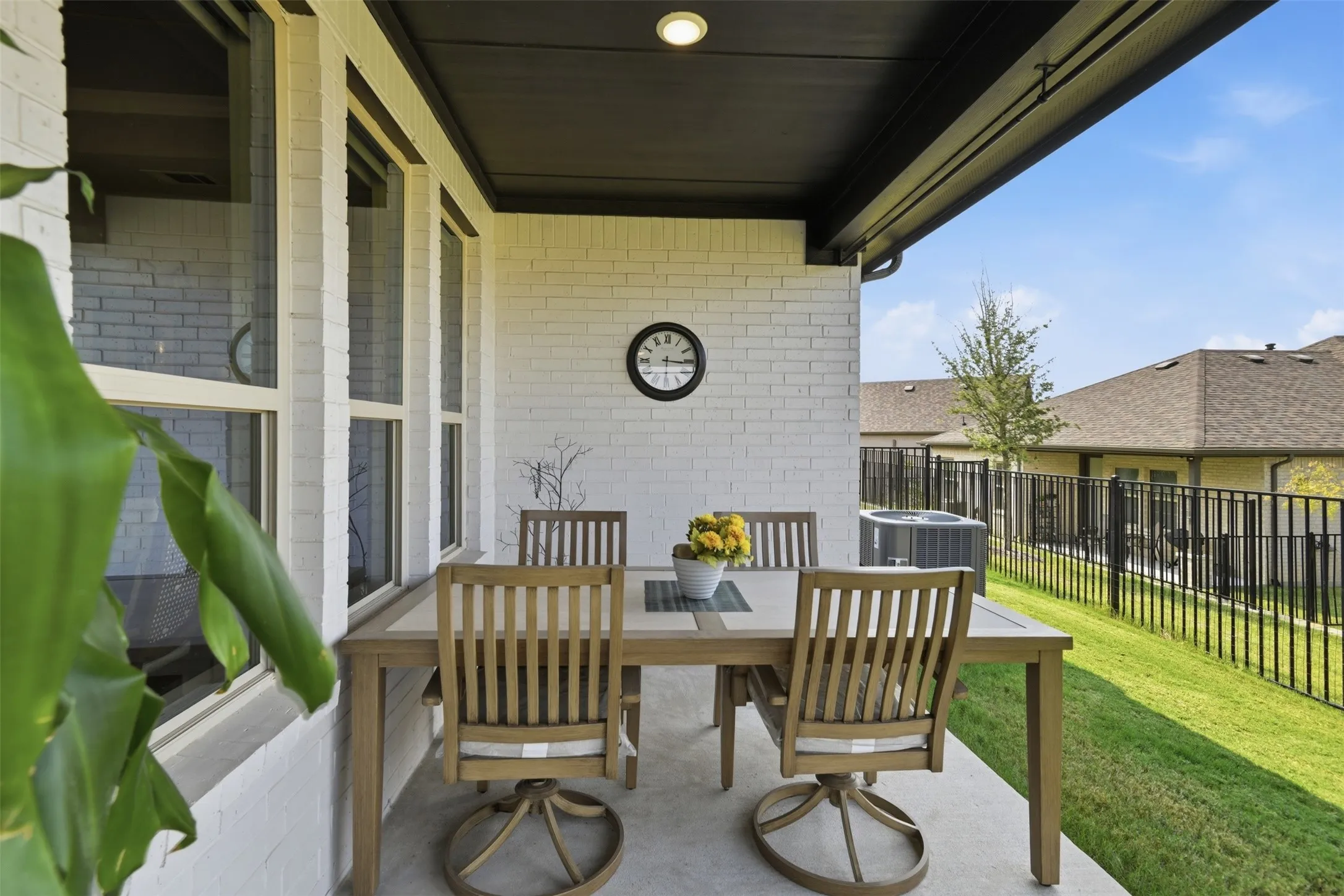 Covered patio featuring a concrete surface, white brick exterior, dark ceiling, and a manicured lawn beyond a black fence
