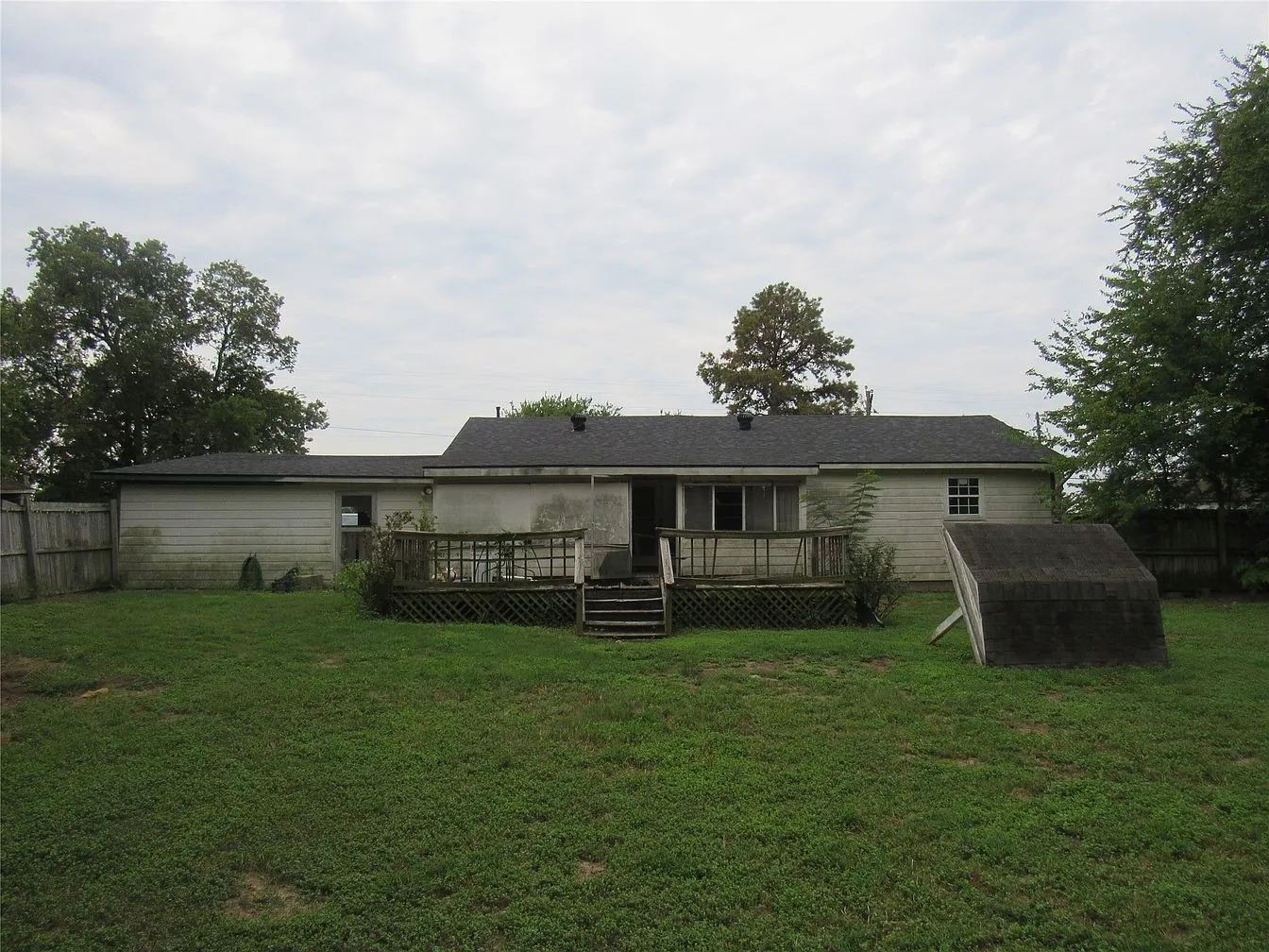 Rear exterior with a wooden deck, sloped roofline, and fenced perimeter
