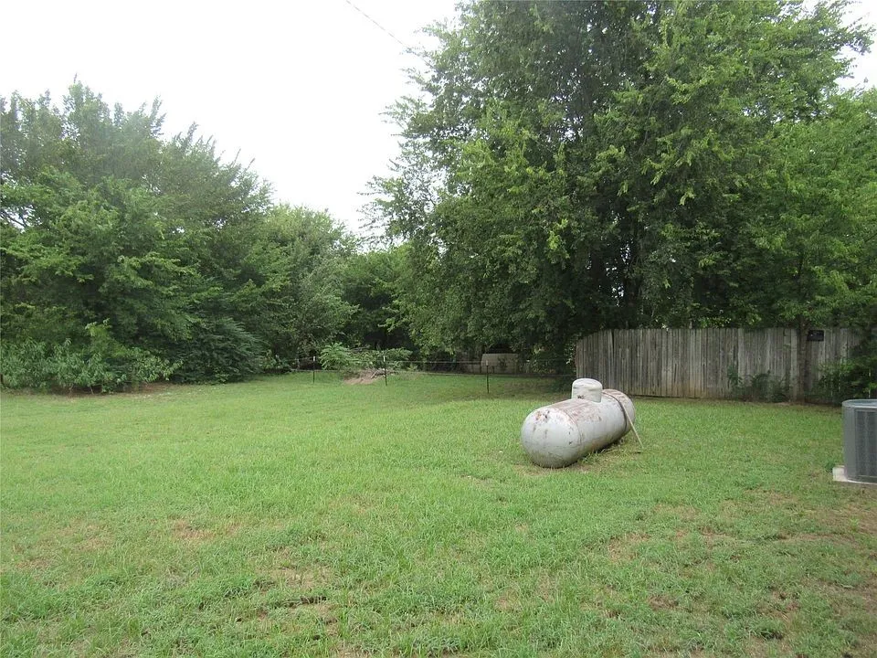 Expansive grassy yard with mature perimeter trees and a wood fence