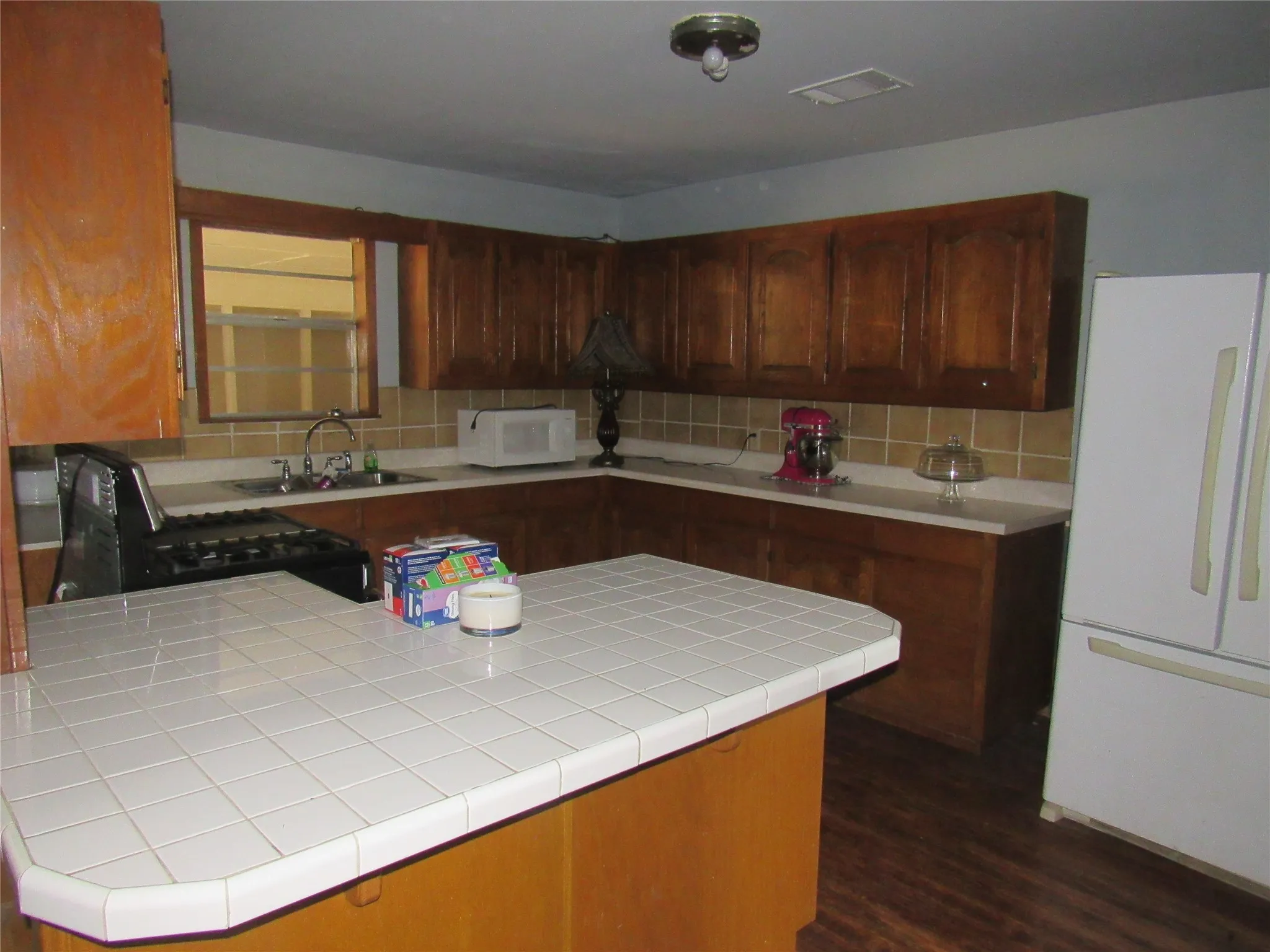 Kitchen featuring wood-finish cabinetry, tile countertops, an integrated sink, and wood-finish flooring