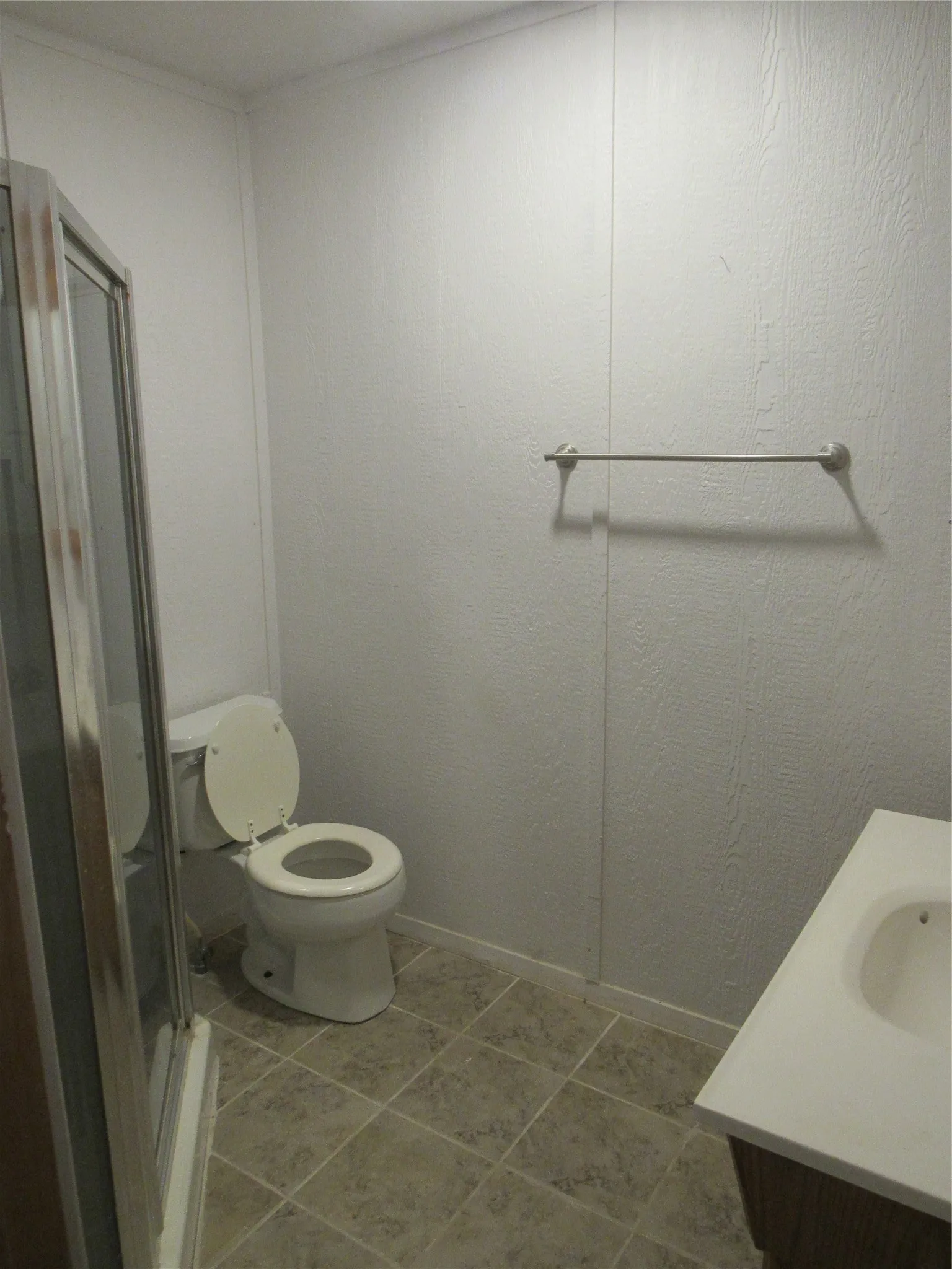 Shower enclosure with clear glass panel, toilet, vanity with integrated sink, and tiled flooring