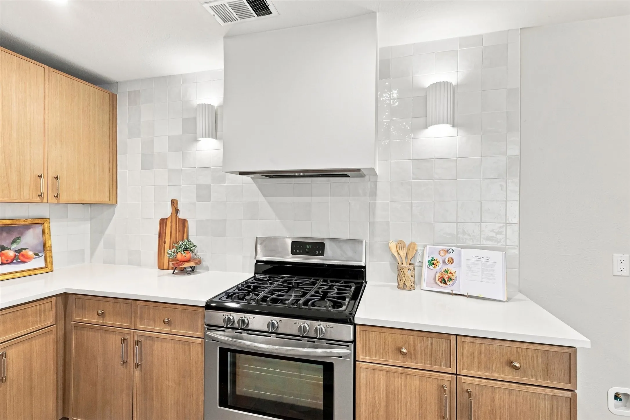 Modern kitchen featuring warm wood-finish cabinetry, white subway tile backsplash, stainless steel gas range with convection oven, and white quartz countertops with ample workspace and storage throughout