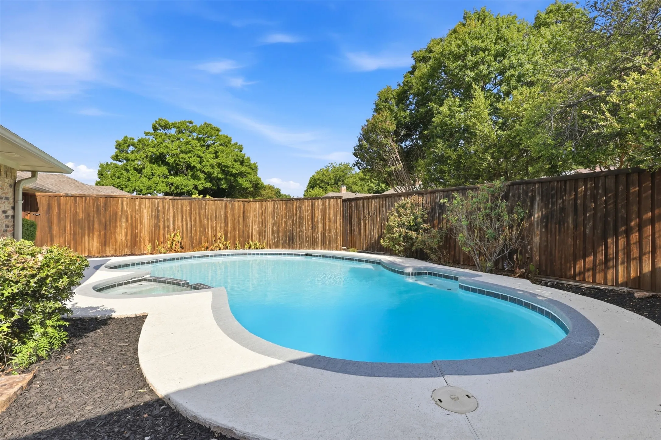 Resort-style pool with integrated spa, concrete decking, and wood privacy fencing